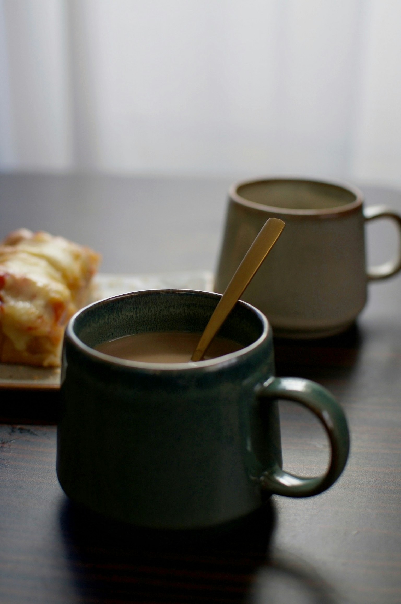 Cangkir hijau dengan kopi dan sendok di samping cangkir berwarna terang dan kue di latar belakang