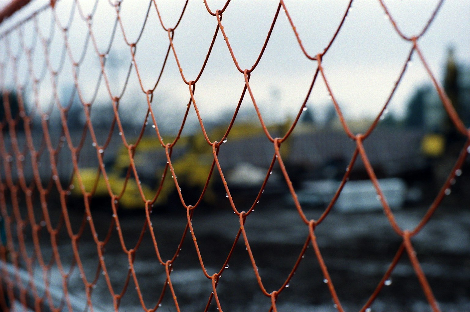 Close-up of a rusty wire fence with raindrops background featuring a blurred construction site
