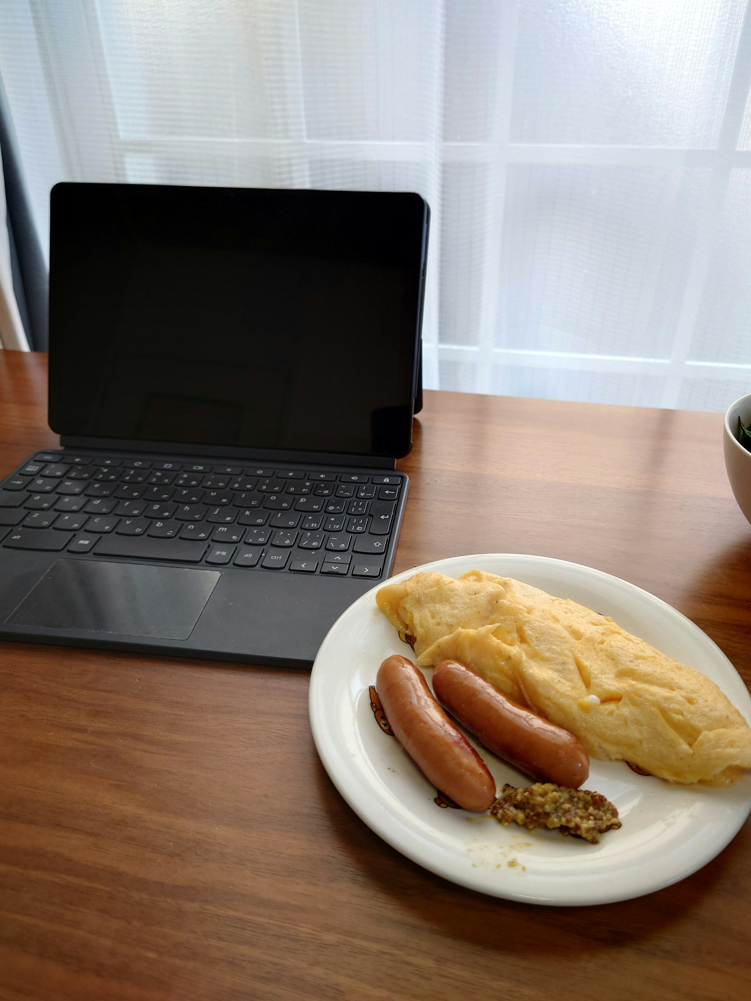 Piring berisi sosis dan omelet di atas meja kayu di samping tablet dan mangkuk salad