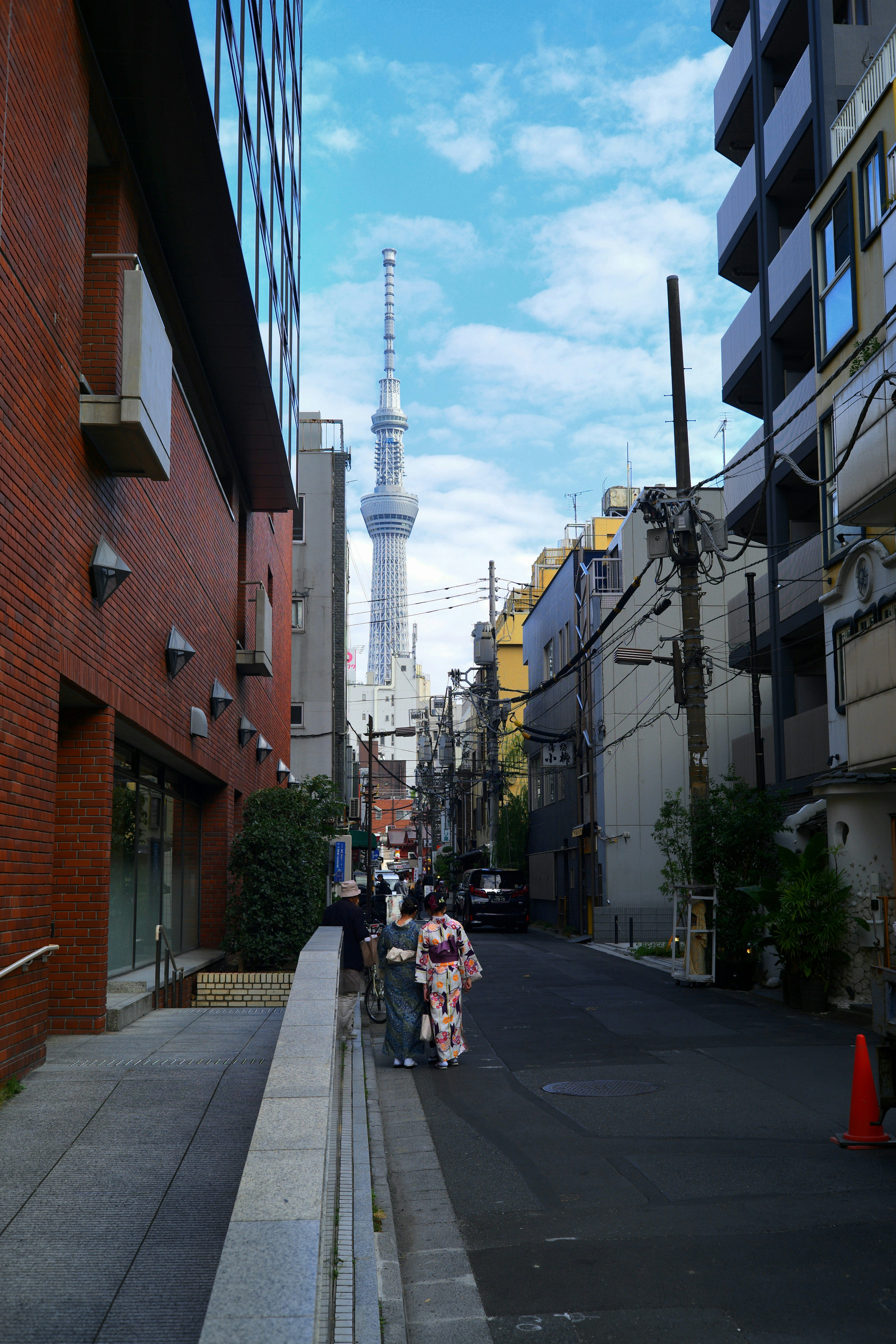路地を歩く人々と東京スカイツリーが見える街並み