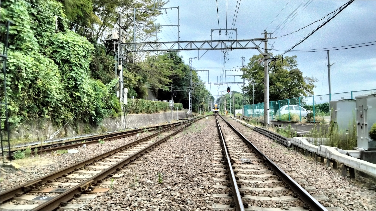 Railway tracks bordered by lush greenery and a cloudy sky