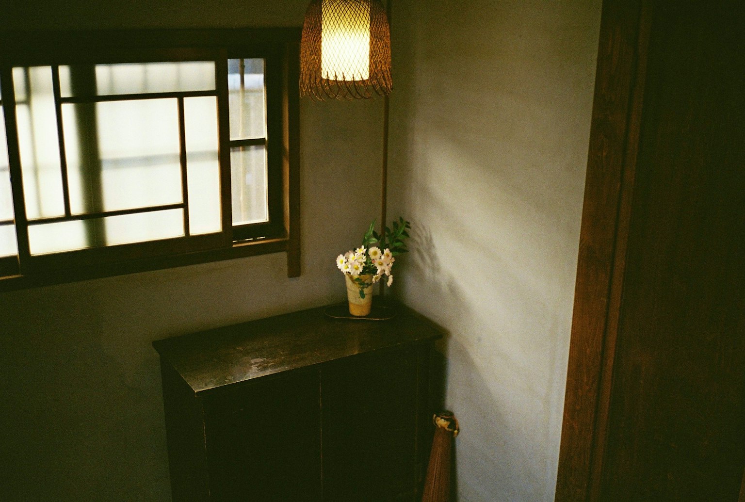 階段の上から見た室内のコーナーにある木製のキャビネットと花瓶の花がある