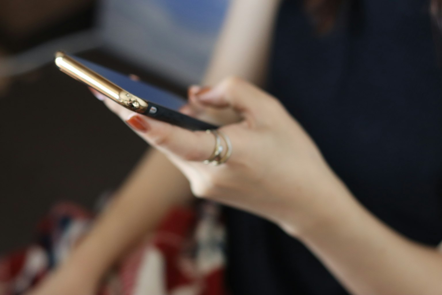 Primer plano de una mano sosteniendo un smartphone con marco dorado y uñas rojas