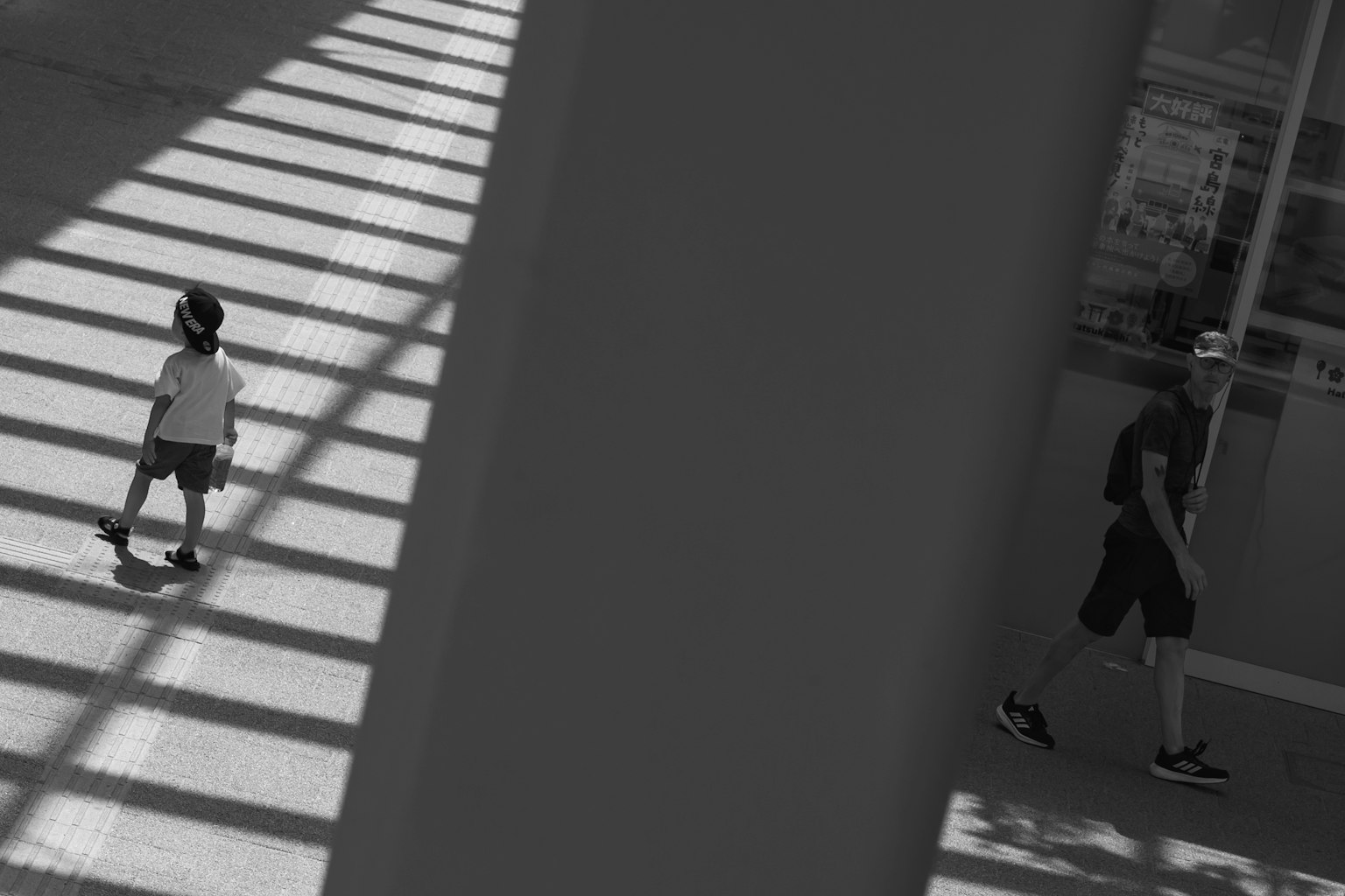 Schwarzweißfoto eines Kindes und eines Erwachsenen, die durch gestreifte Schatten auf dem Boden gehen