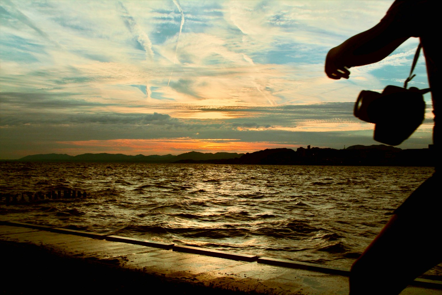 Silhouette di una persona che tiene una macchina fotografica contro un tramonto con acqua increspata
