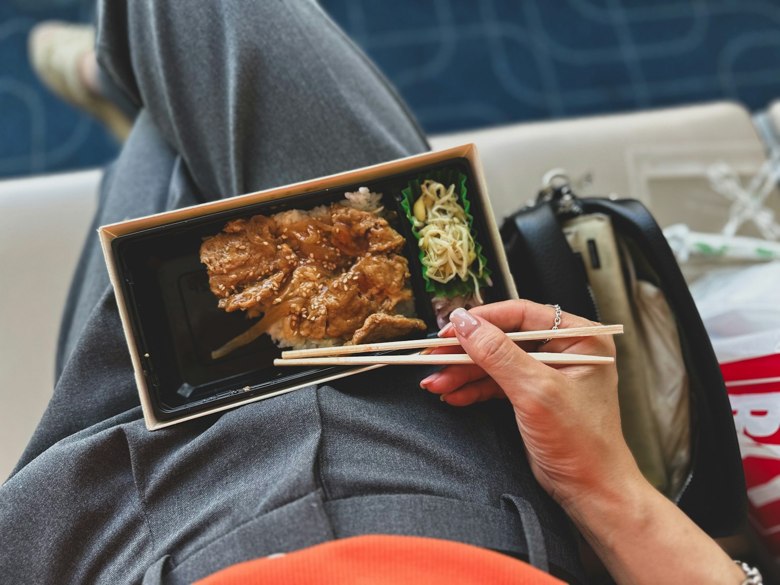 Mano che tiene una scatola bento con tonkatsu croccante e noodles mentre indossa pantaloni sportivi