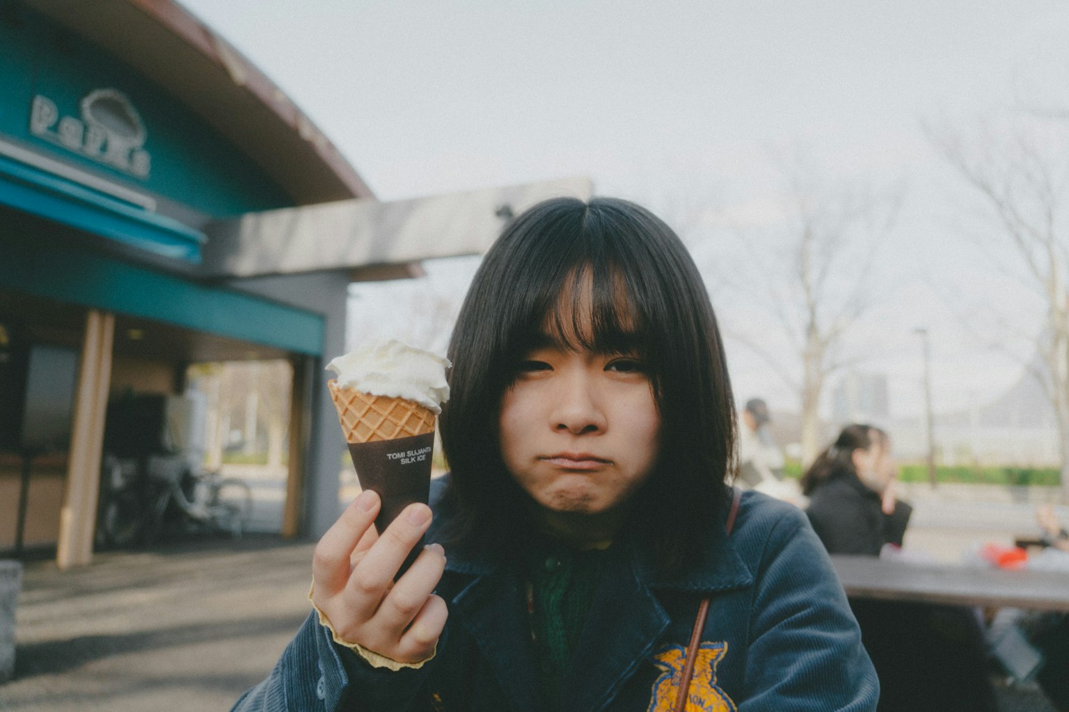 黑发女孩手拿冰淇淋甜筒，表情不满