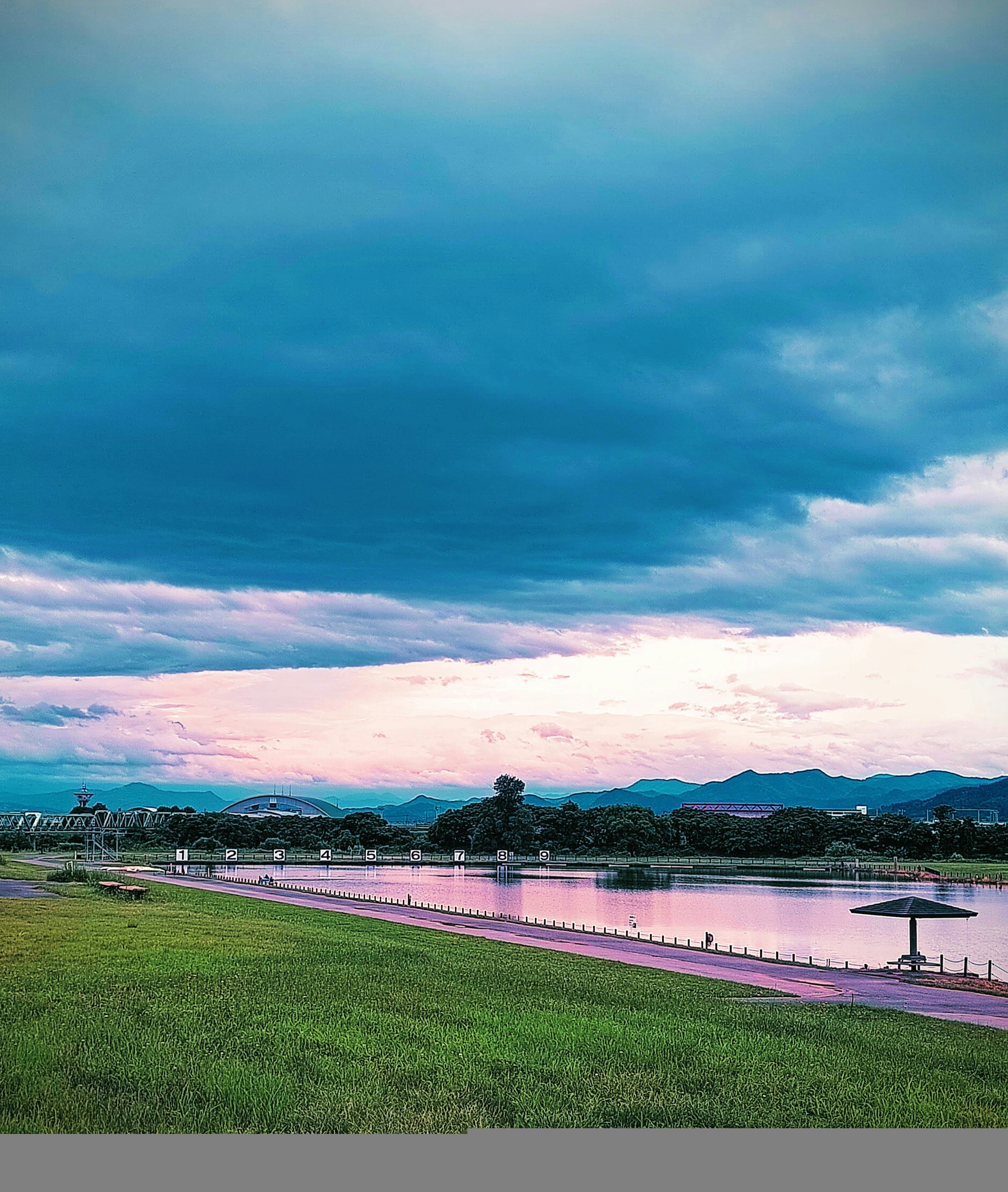 夕暮れの漕艇場でカヌーが浮かぶ水面と芝生の岸辺