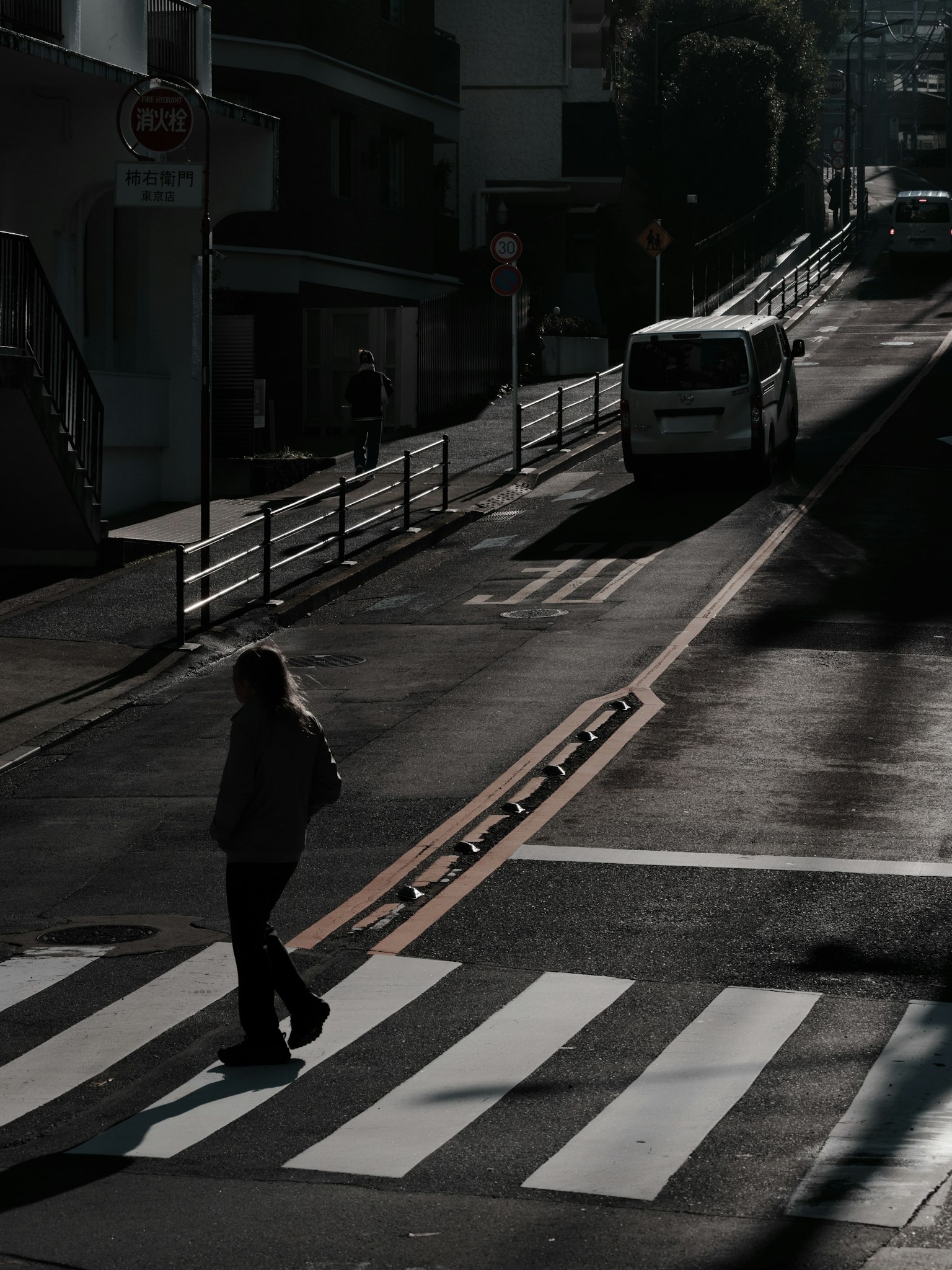 A person crossing a dark street with a vehicle in the background