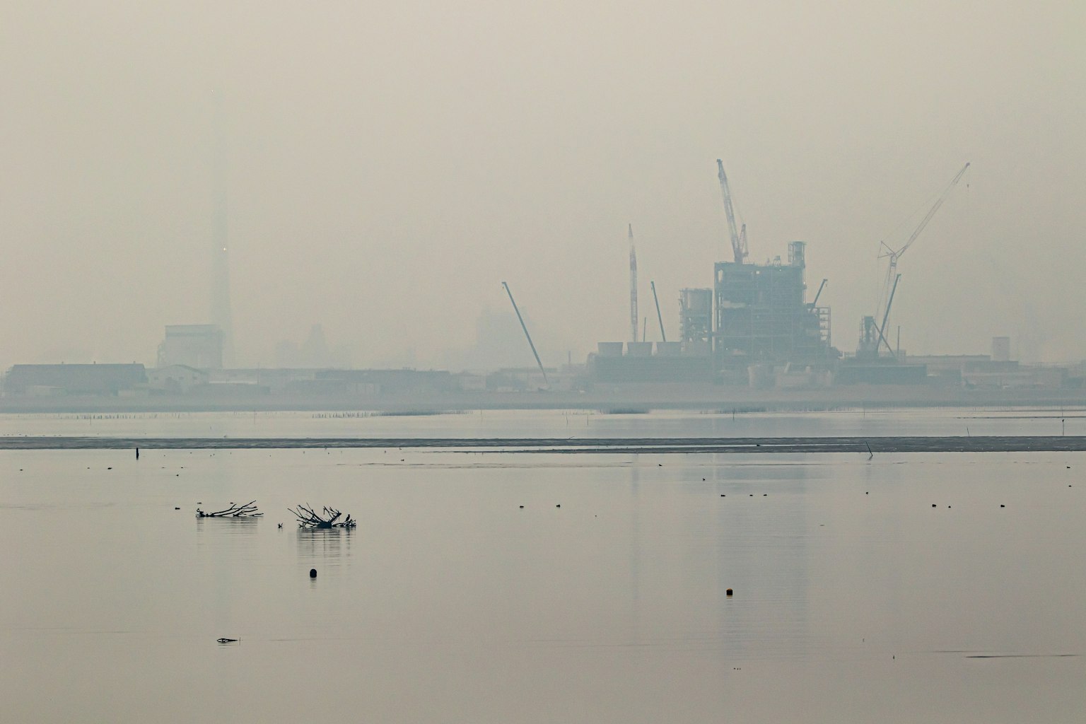Instalación industrial envuelta en niebla con reflejos en el agua