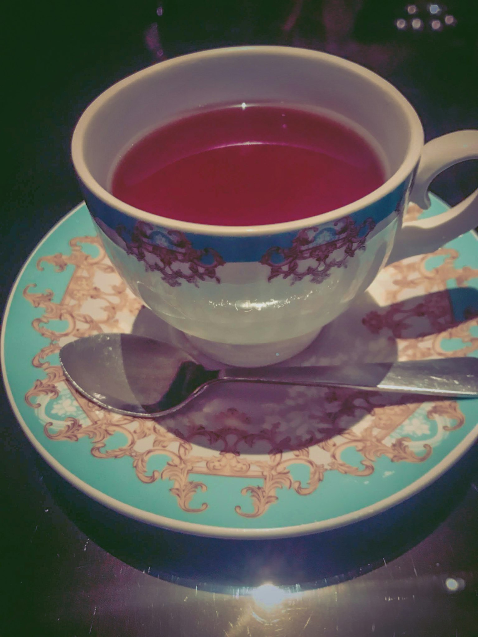 Une tasse de thé rouge posée sur une soucoupe bleue avec une cuillère en argent