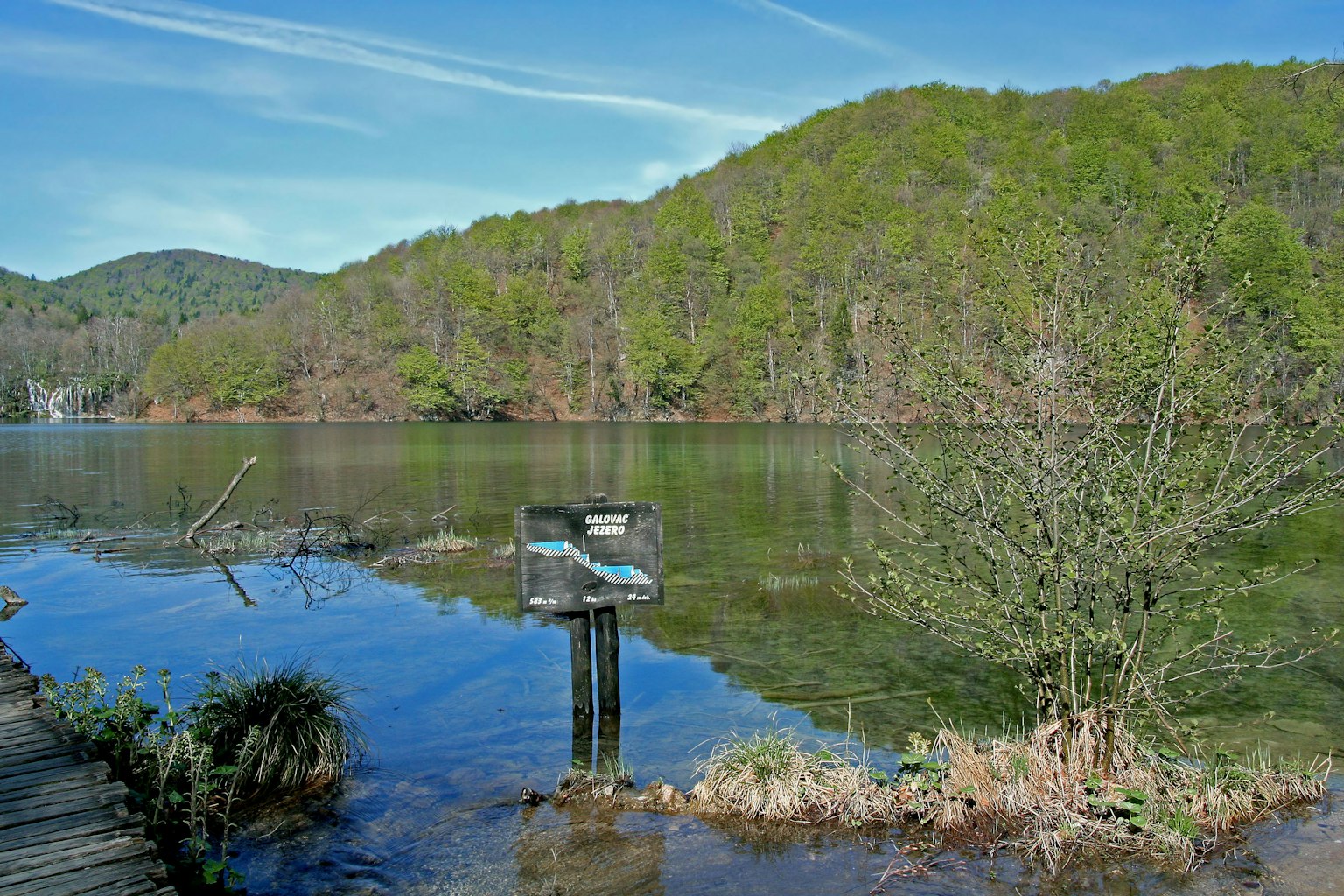 Vista panoramica di un lago con un cartello e colline verdi sullo sfondo
