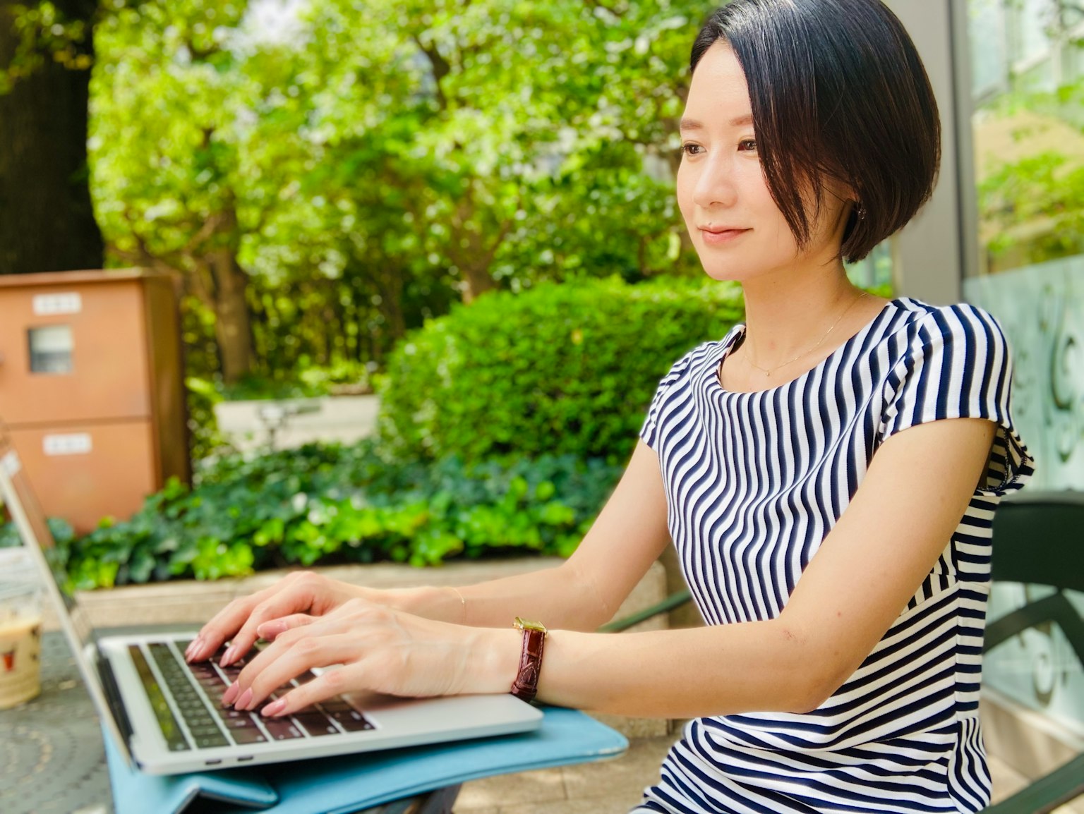 Frau, die in einem Park einen Laptop benutzt grüner Hintergrund und gestreiftes Shirt