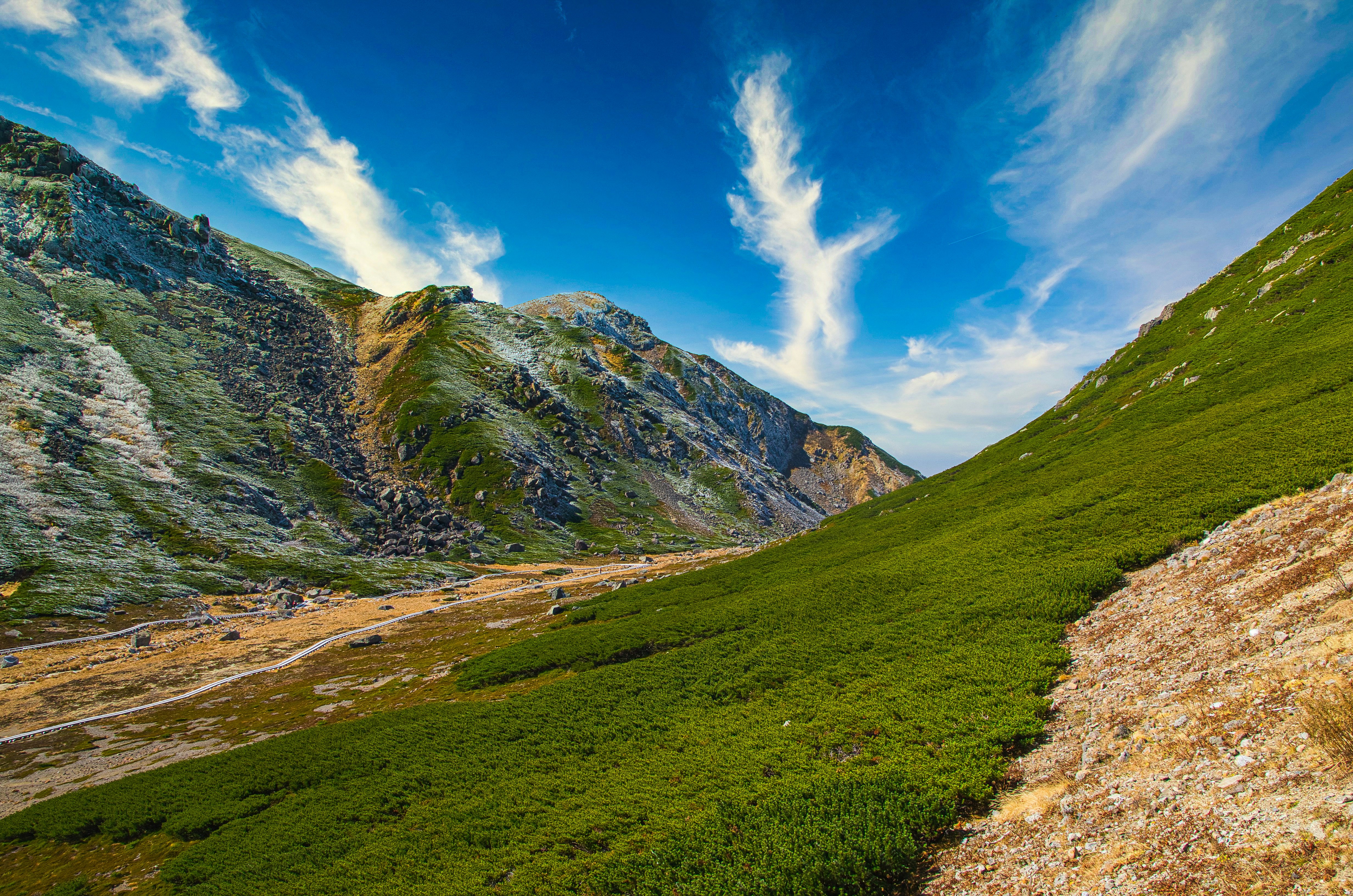 sentier de montagne vert et vallée rocheuse sous un ciel bleu