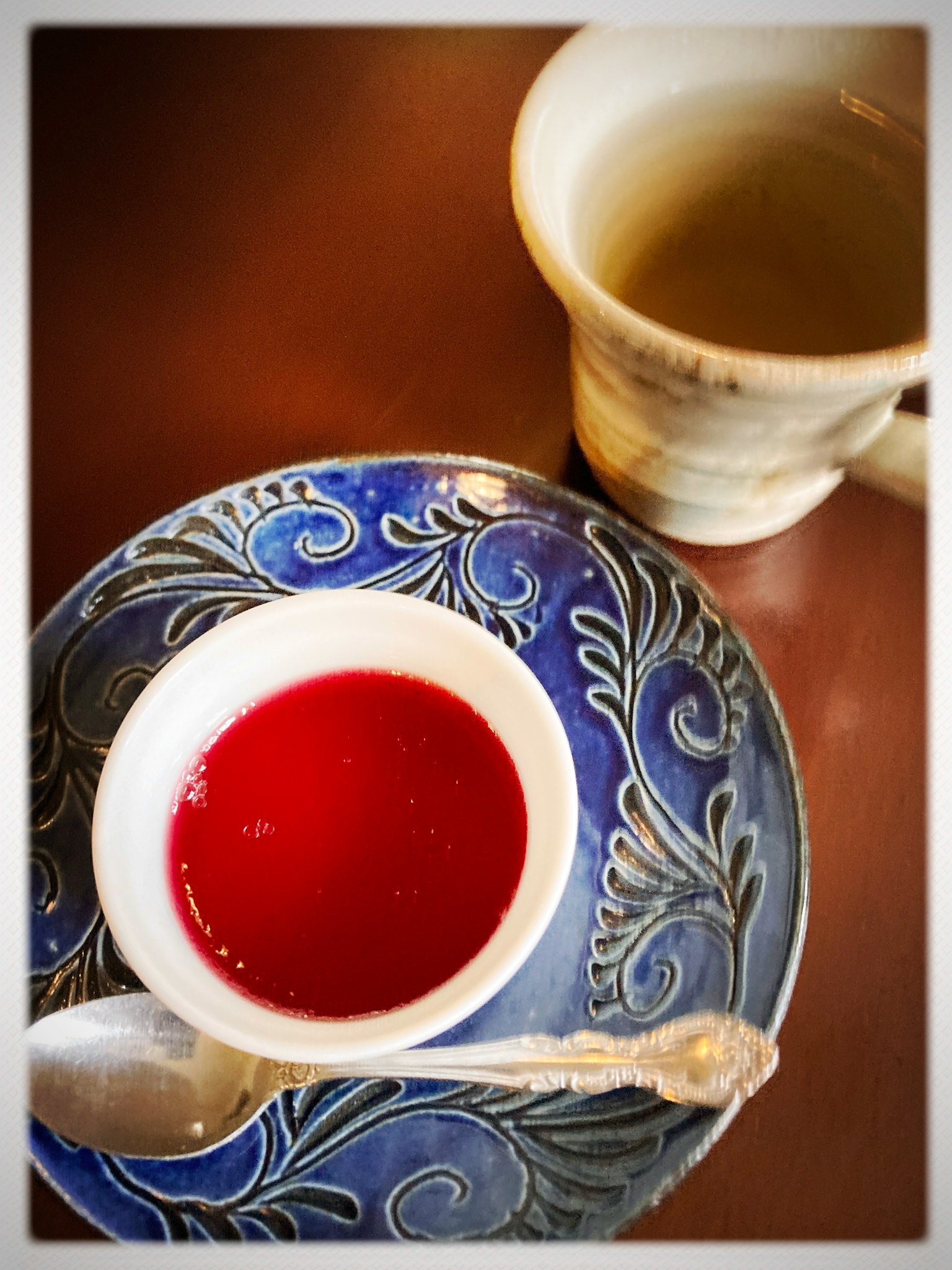 青い皿に赤いゼリーとスプーンが置かれたテーブルの上に、白いカップに入ったお茶がある