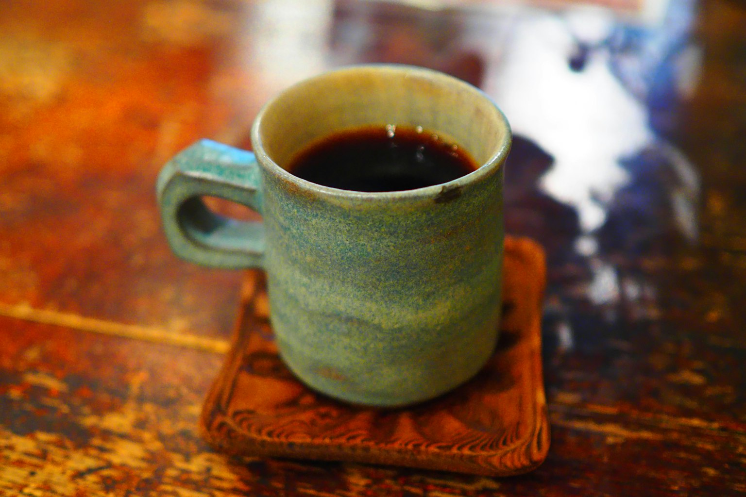 藍色陶瓷咖啡杯放在木質杯墊上， resting 在桌子上