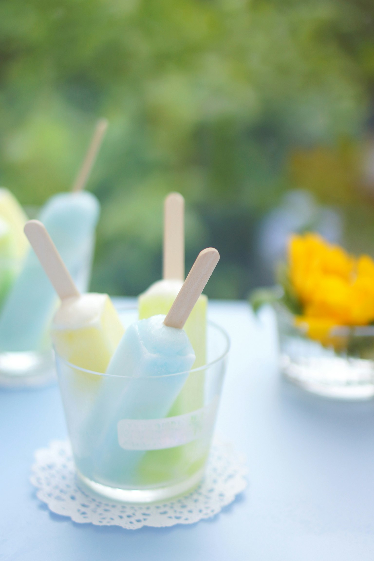 Dos paletas azules y verdes en un vaso con una flor al fondo