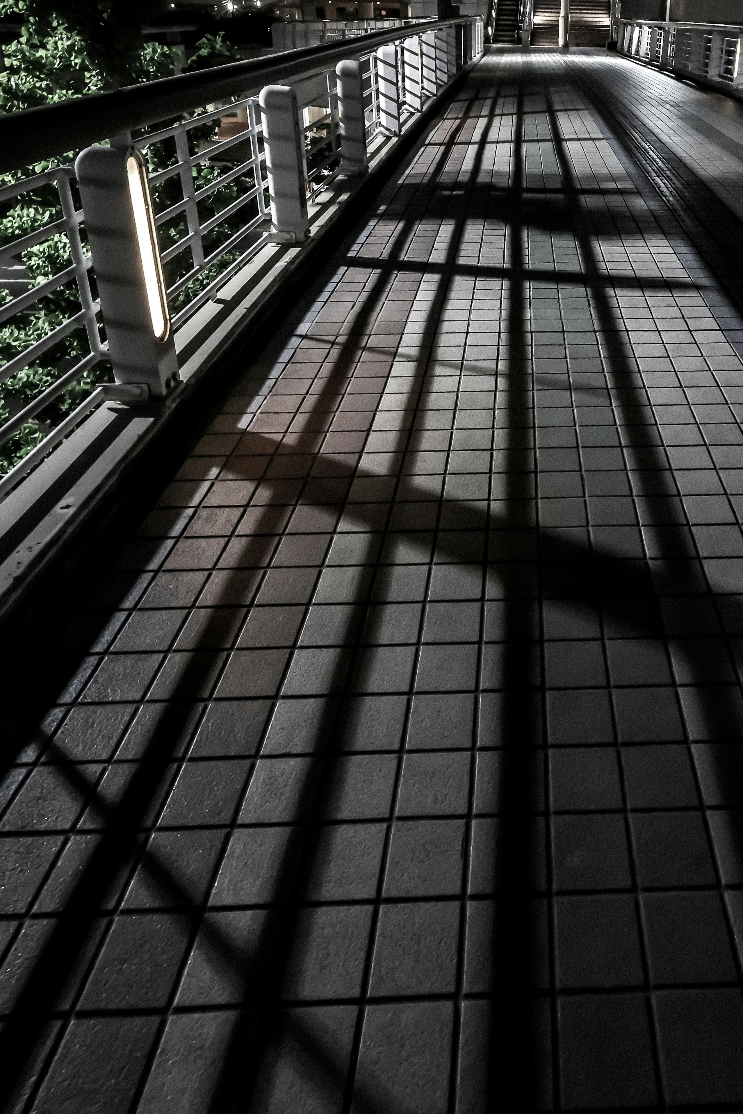 Geländer einer Fußgängerbrücke mit Laternenlicht und Schatten bei Nacht