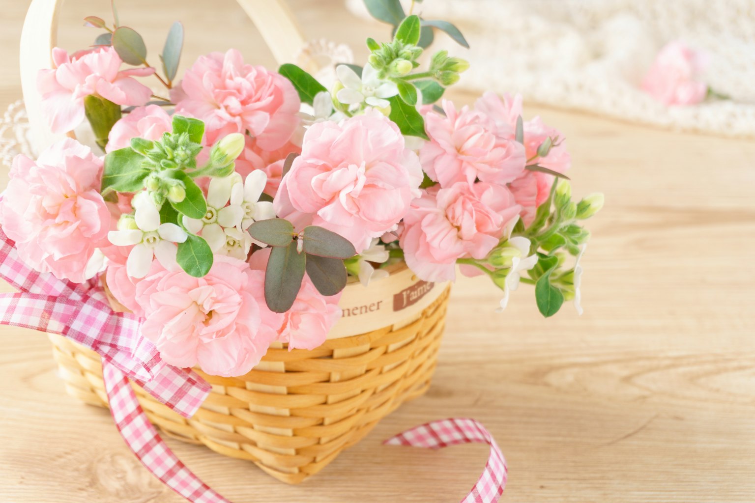 Una cesta llena de flores rosas con un lazo a cuadros