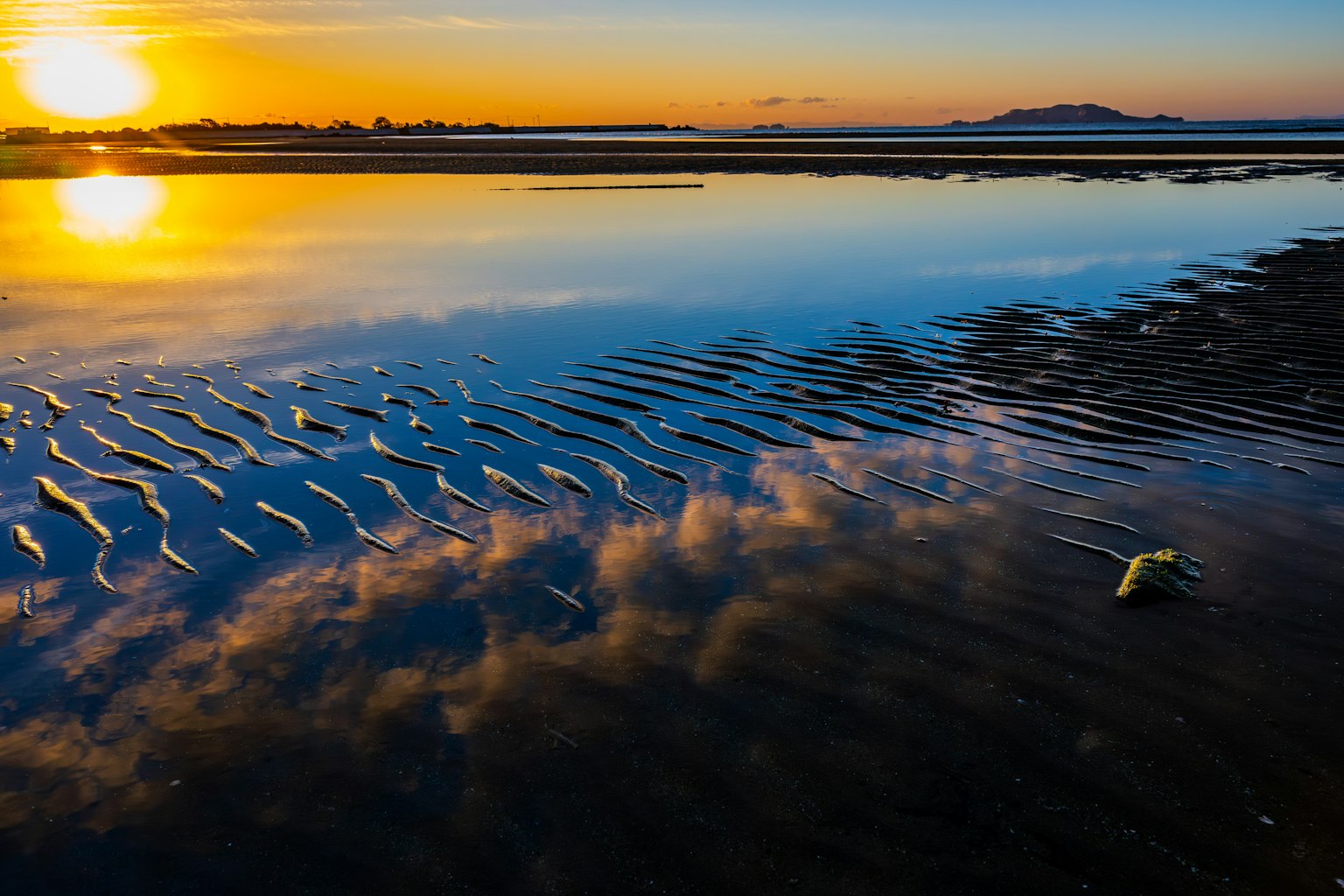 Tramonto che si riflette sulla superficie dell'acqua con sabbia ondulata