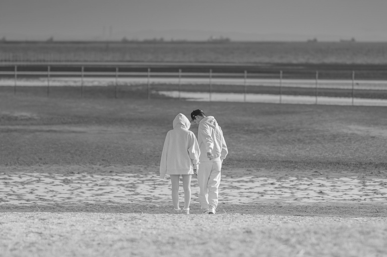 Dos figuras caminando de la mano en una playa en blanco y negro