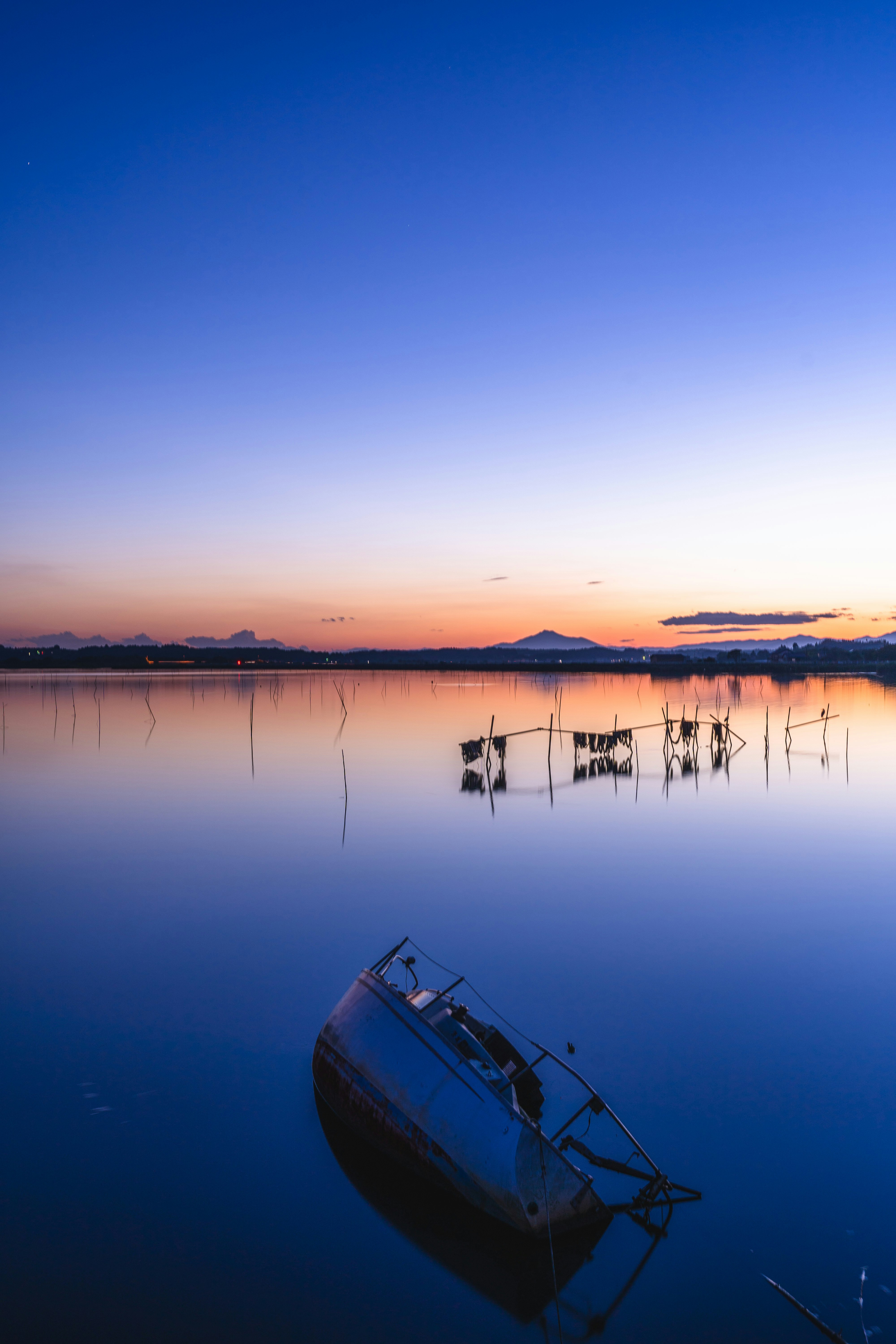 夕暮れの湖面に浮かぶ小舟と静かな水鏡
