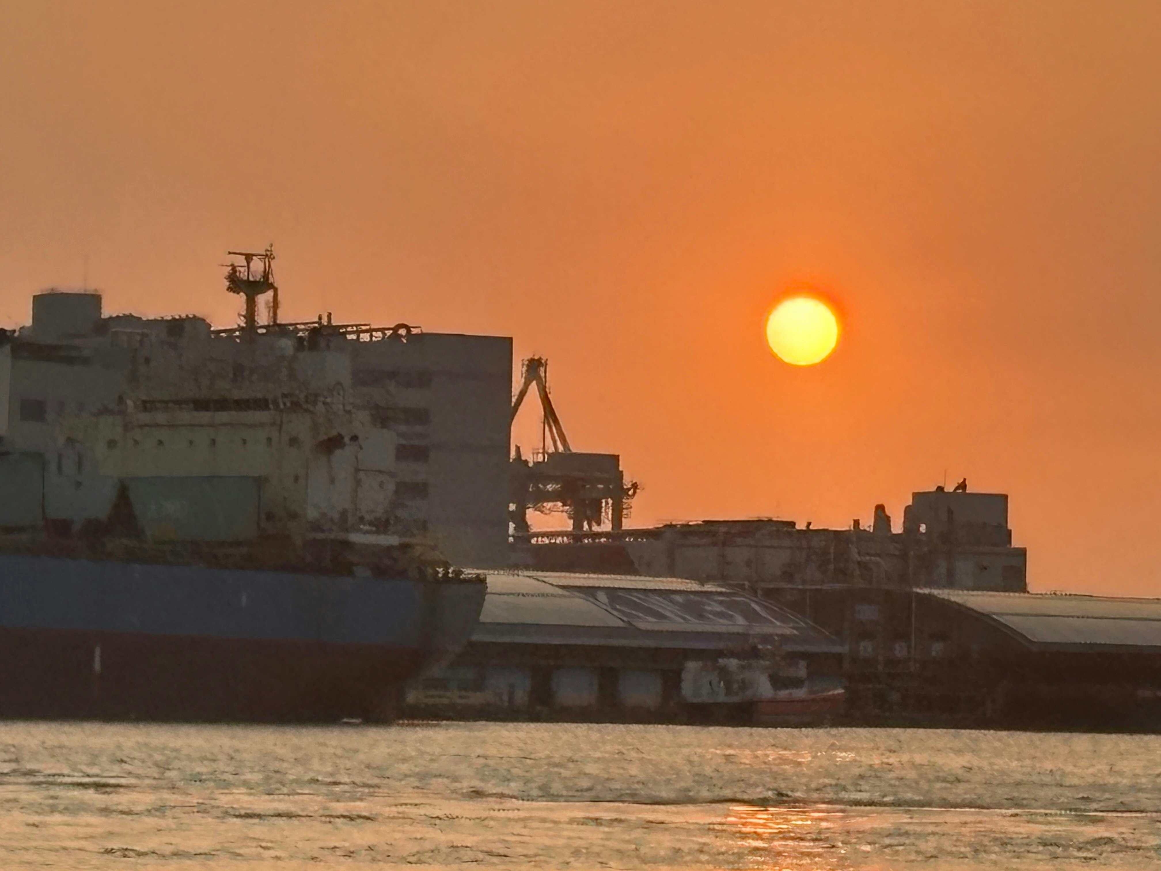 夕暮れの港に停泊する貨物船と夕日