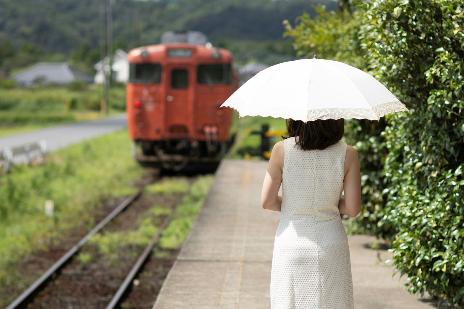 Người phụ nữ cầm ô trắng đứng trước một chiếc tàu đỏ