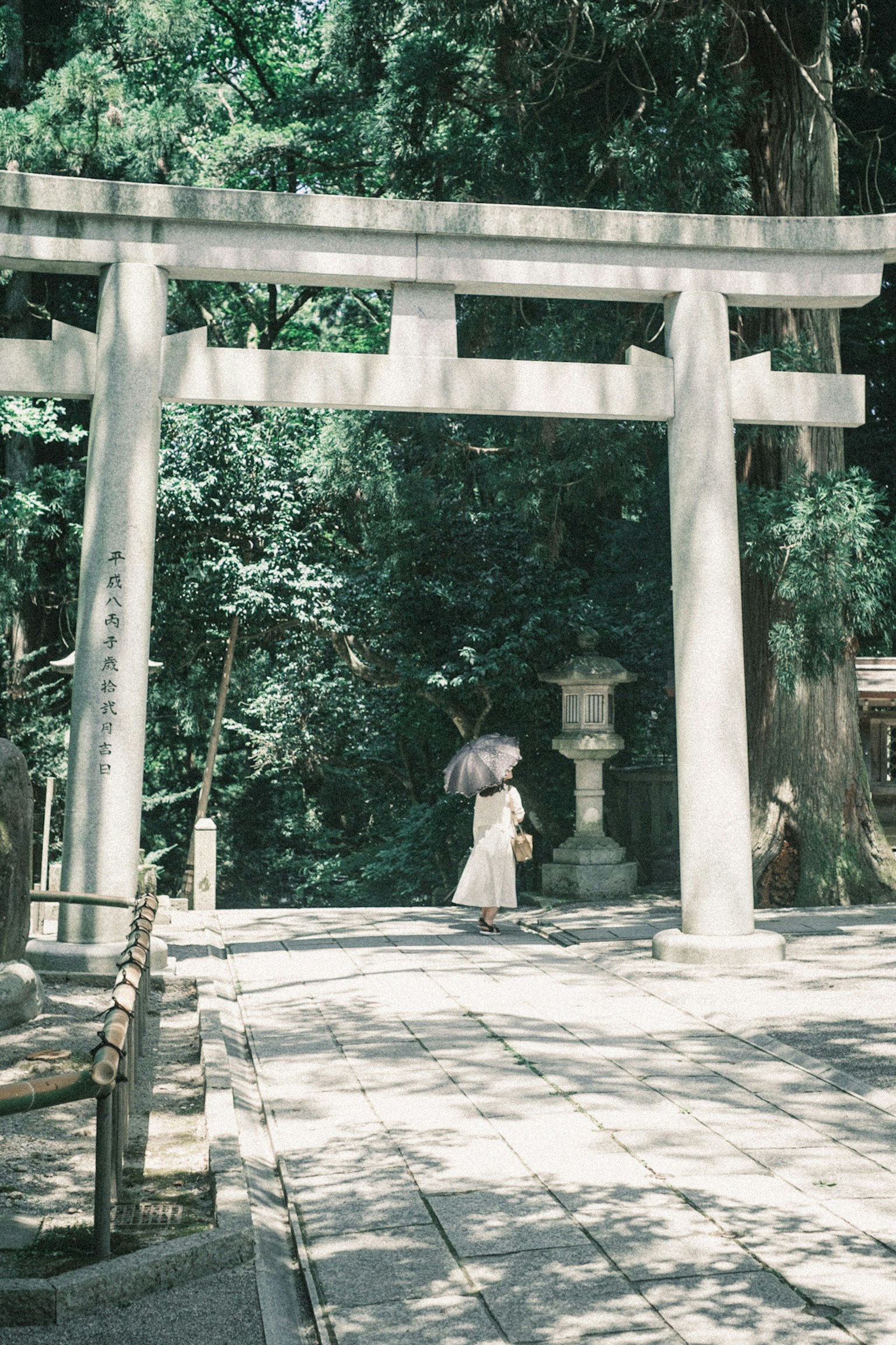 Eine Frau mit einem Regenschirm steht vor einem Torii in einem Schrein