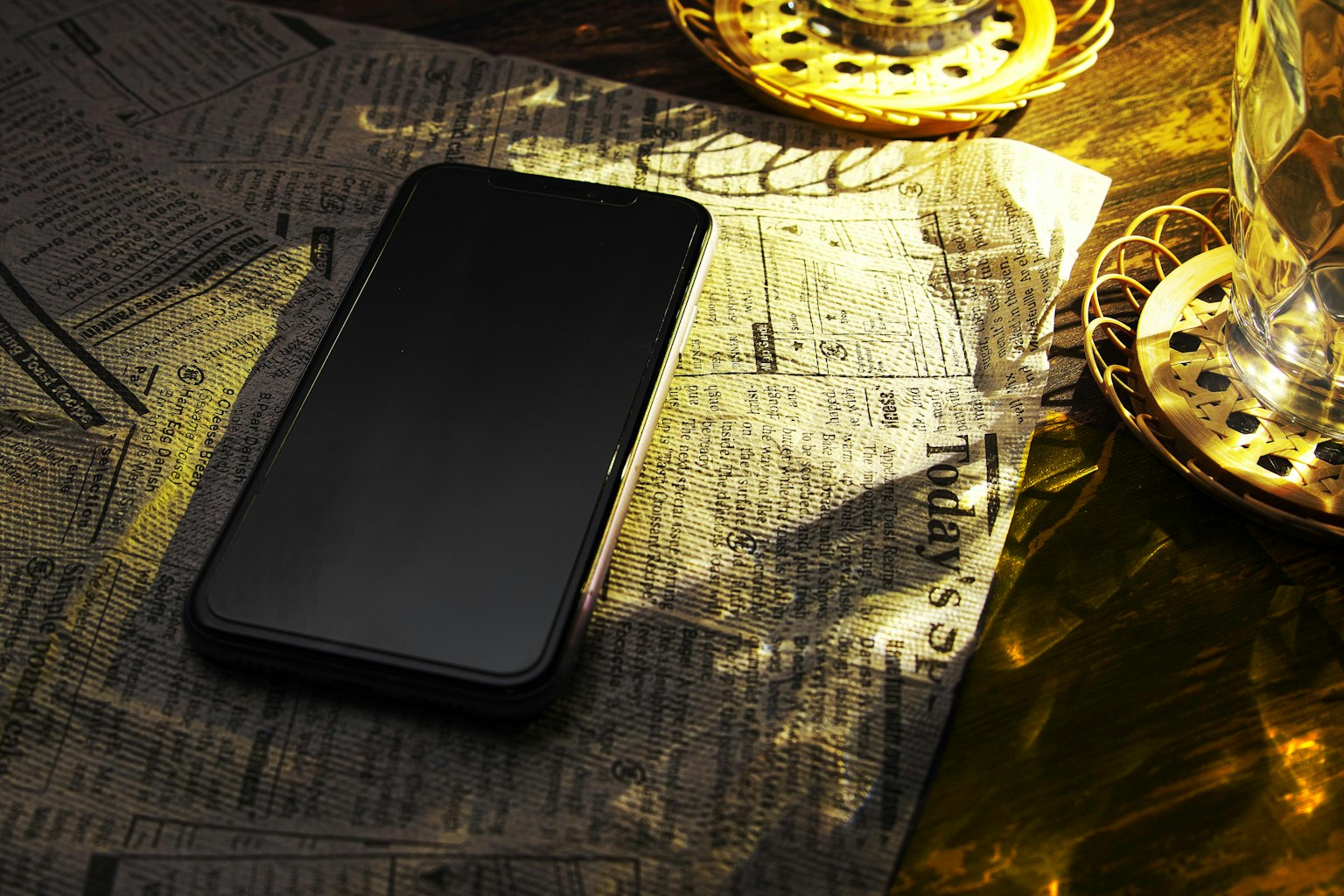 Un smartphone noir posé sur un journal avec des chandeliers dorés en arrière-plan