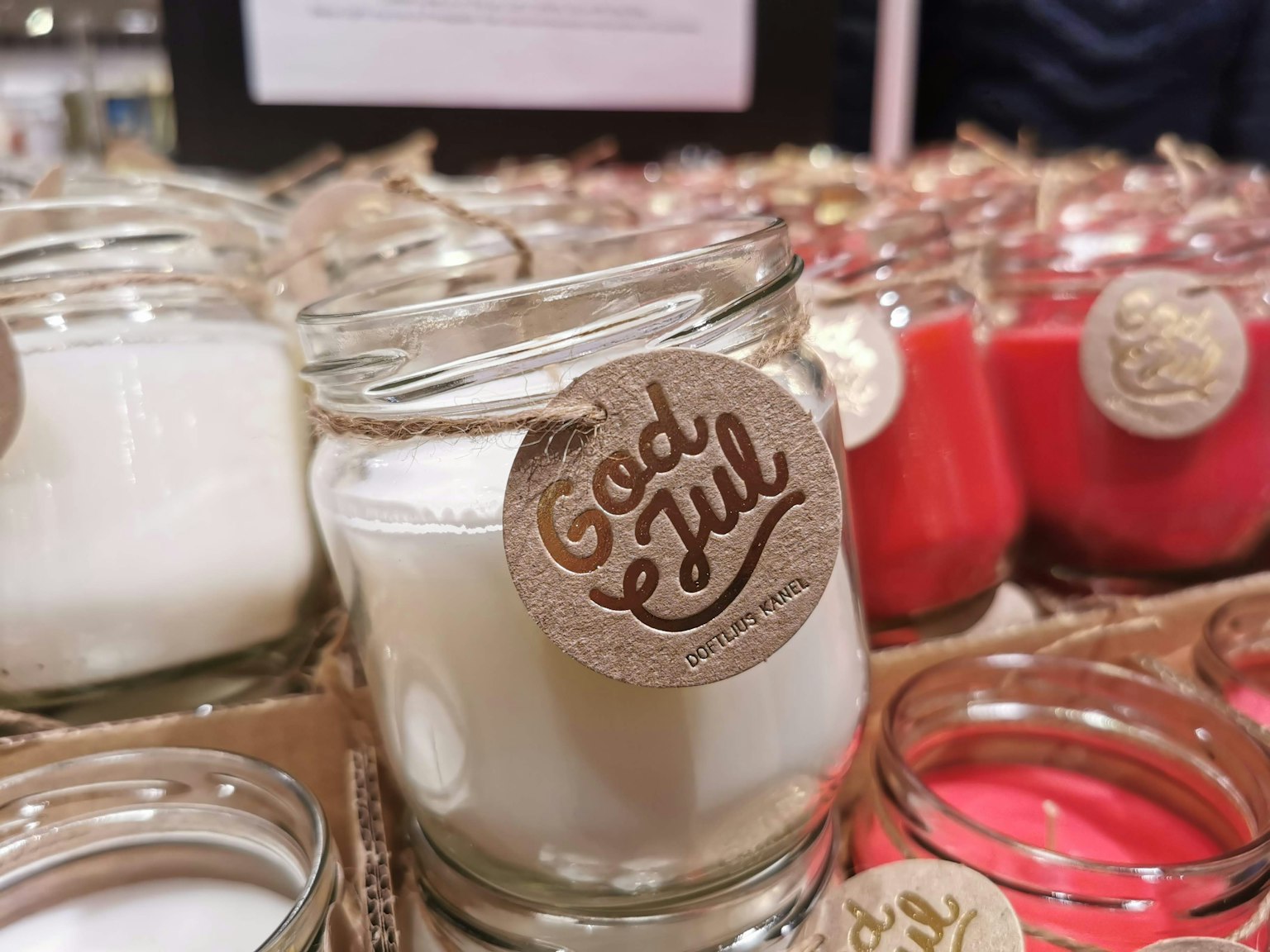 A glass jar with a white candle labeled 'God Jul' among various colored candles