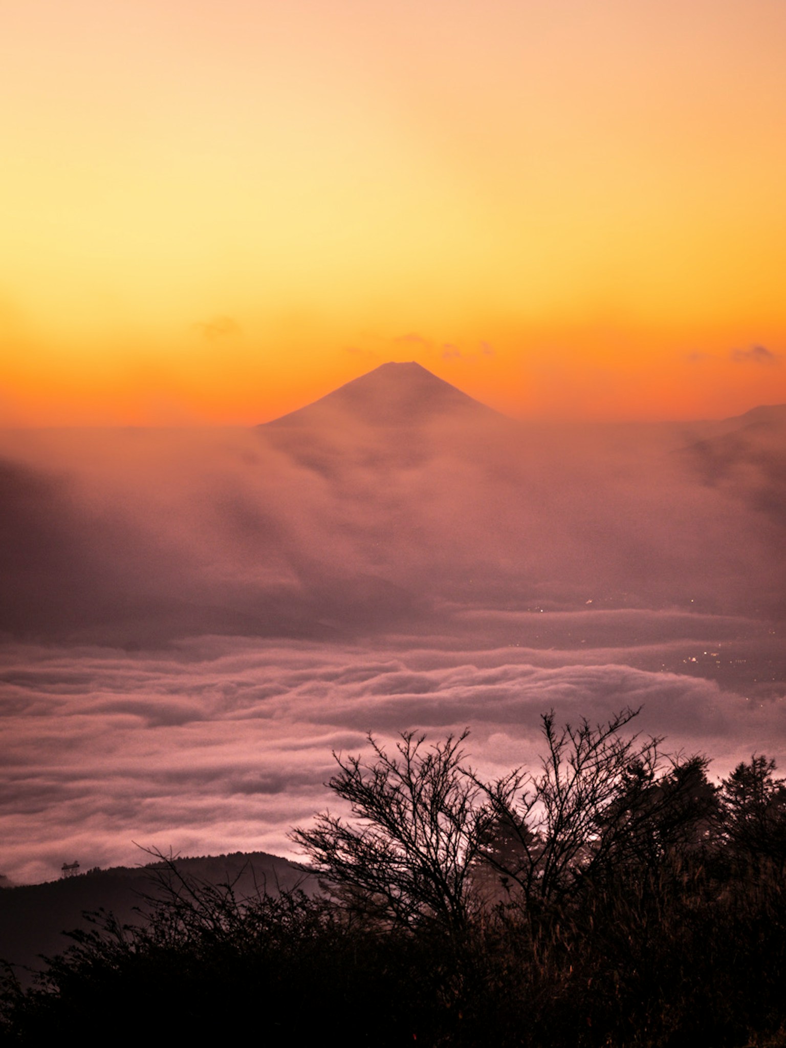 Siluet gunung yang dibungkus kabut dengan matahari terbenam oranye