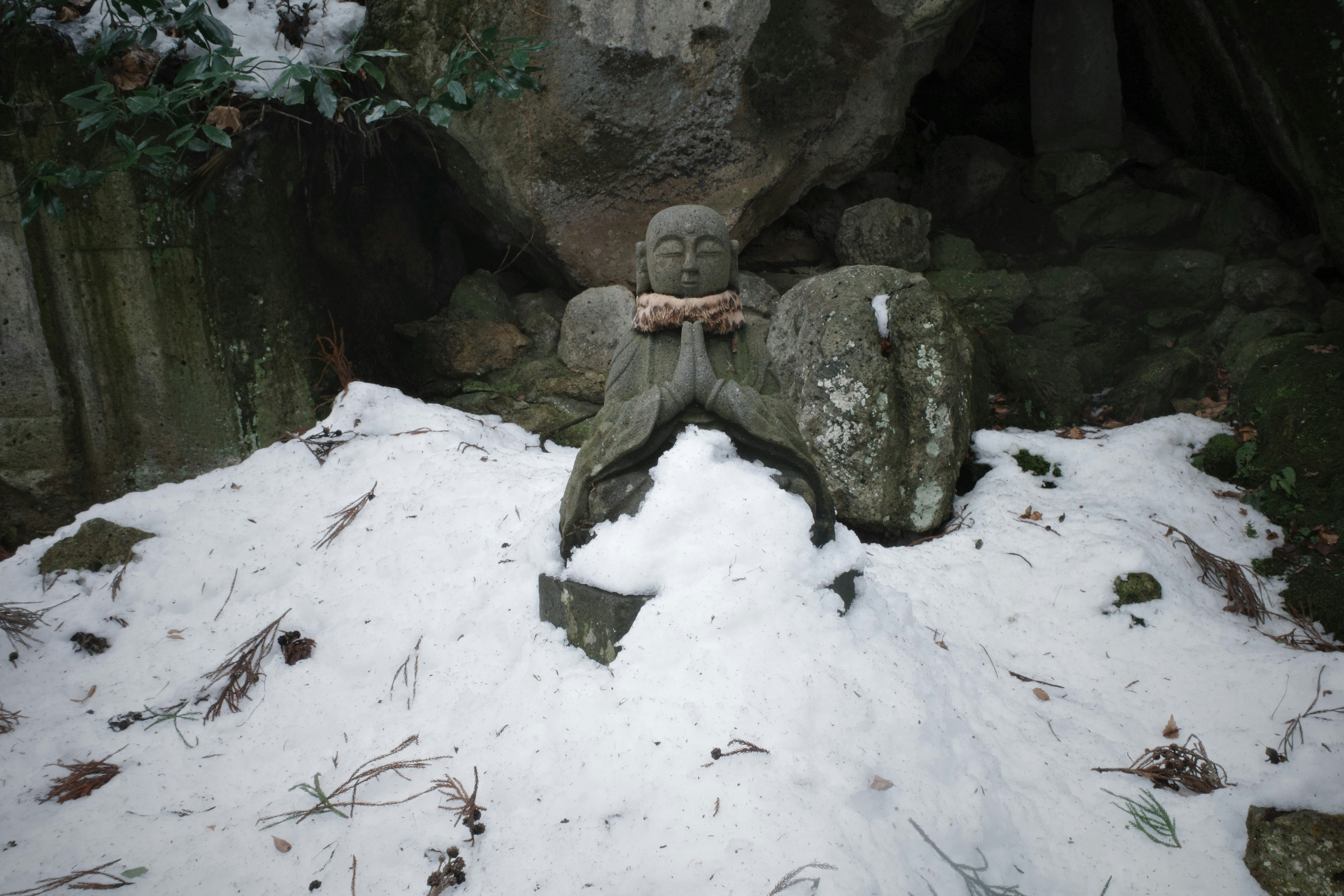 雪の積もった石仏と苔むした石の庭