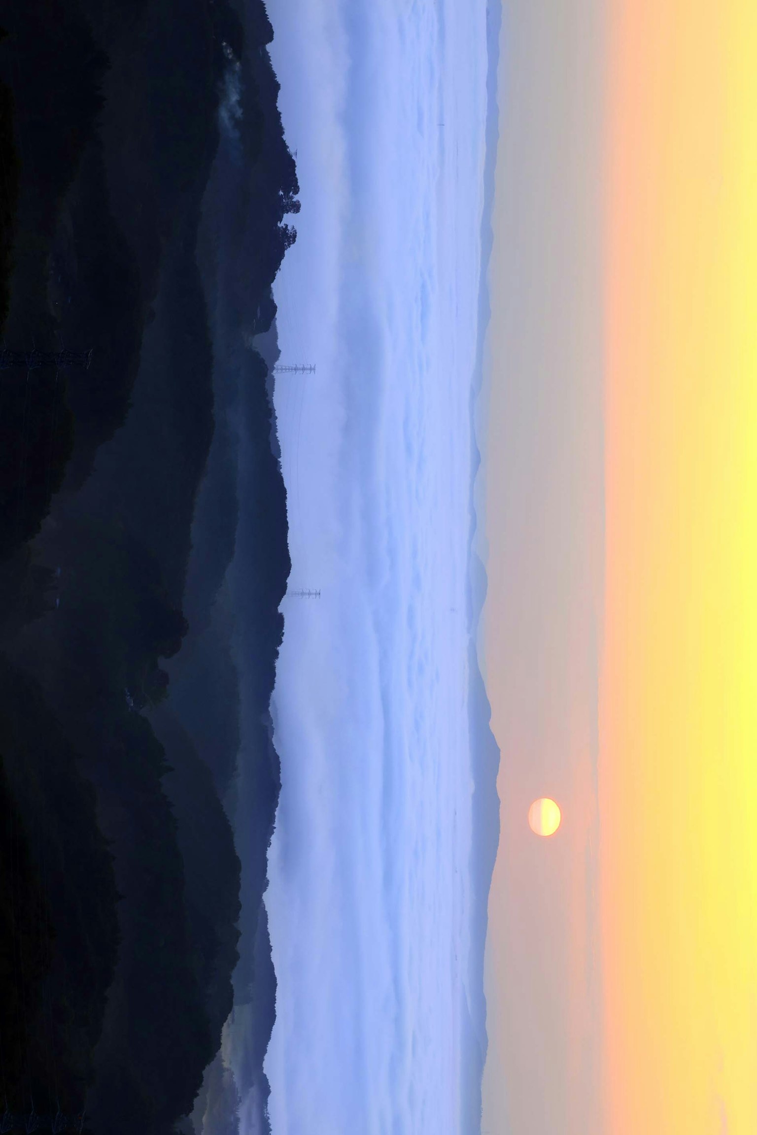 Matahari terbenam di atas awan dengan pegunungan dan langit biru