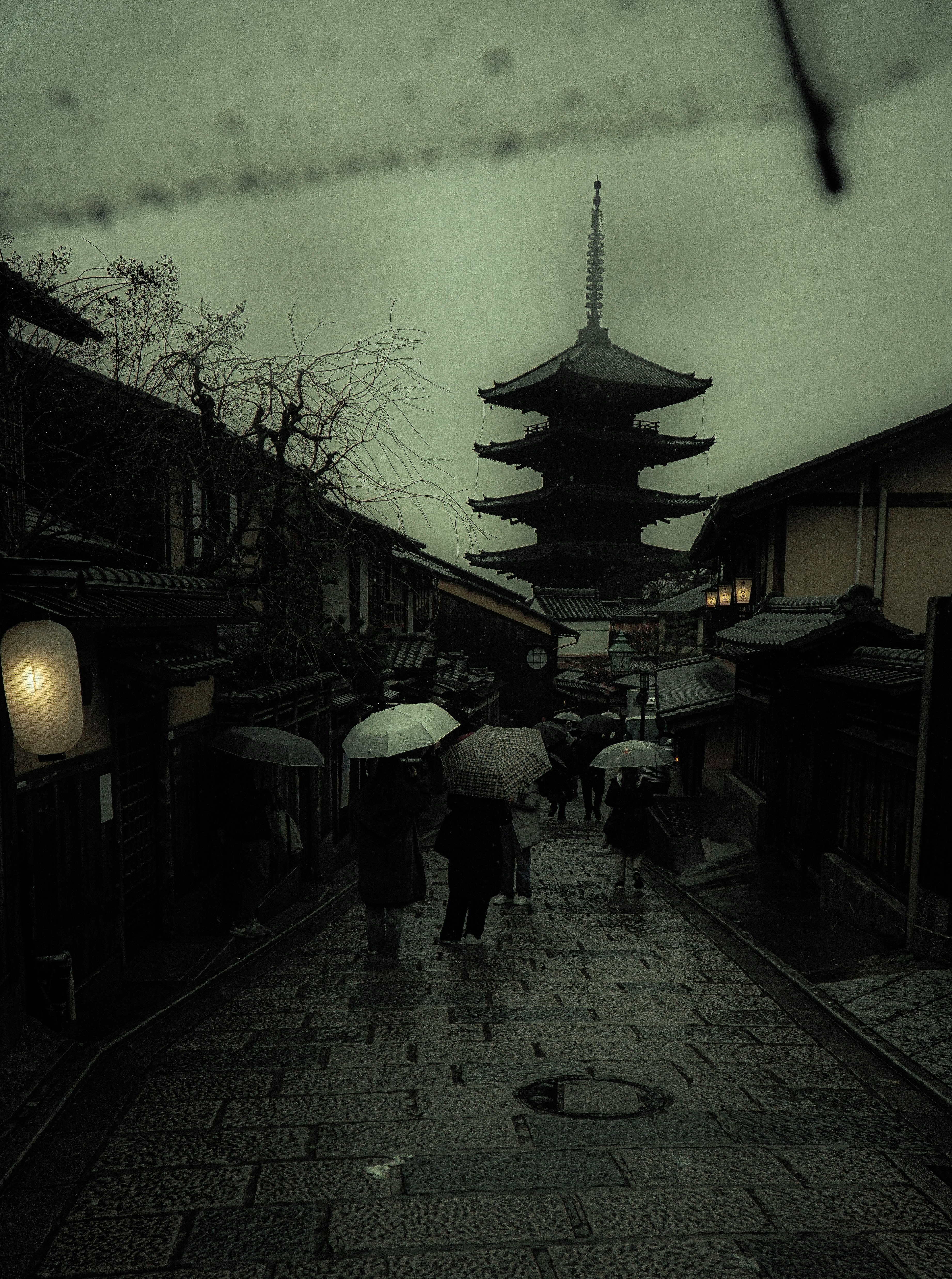 雨上がりの路地に並ぶ提灯と傘、五重塔のある寺院の景観