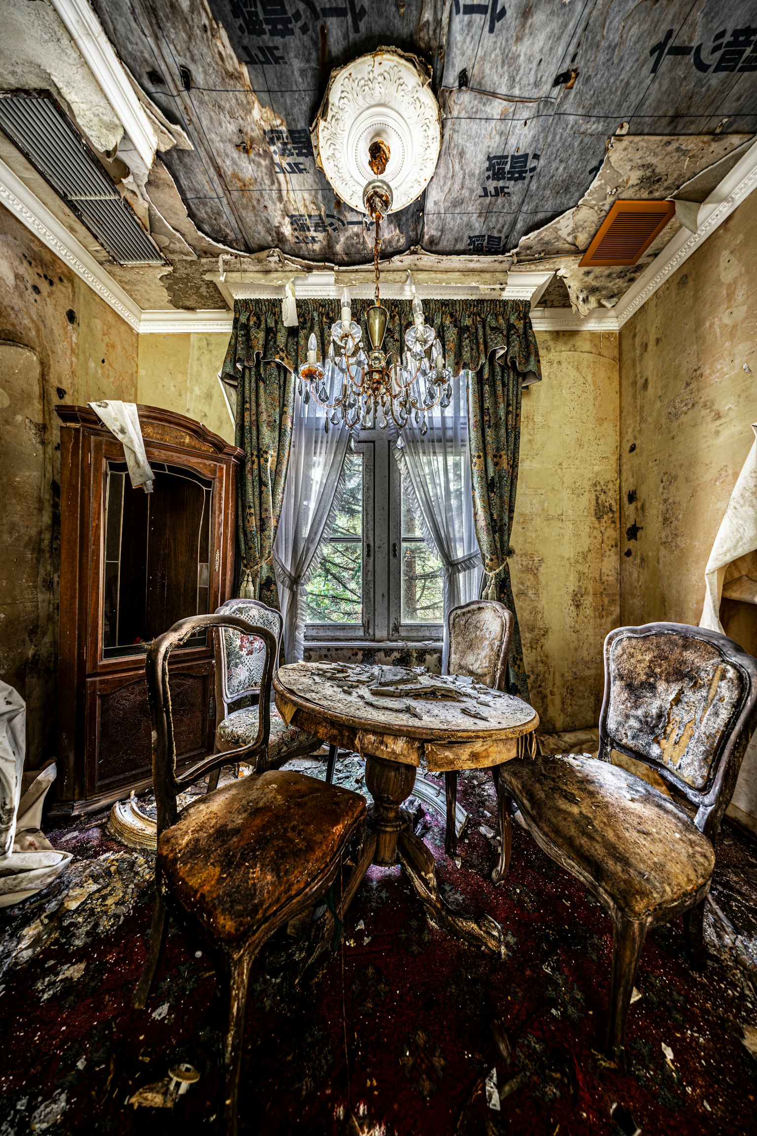 古びた部屋の中にあるテーブルと椅子、シャンデリア、窓からの自然光、壁の剥がれ