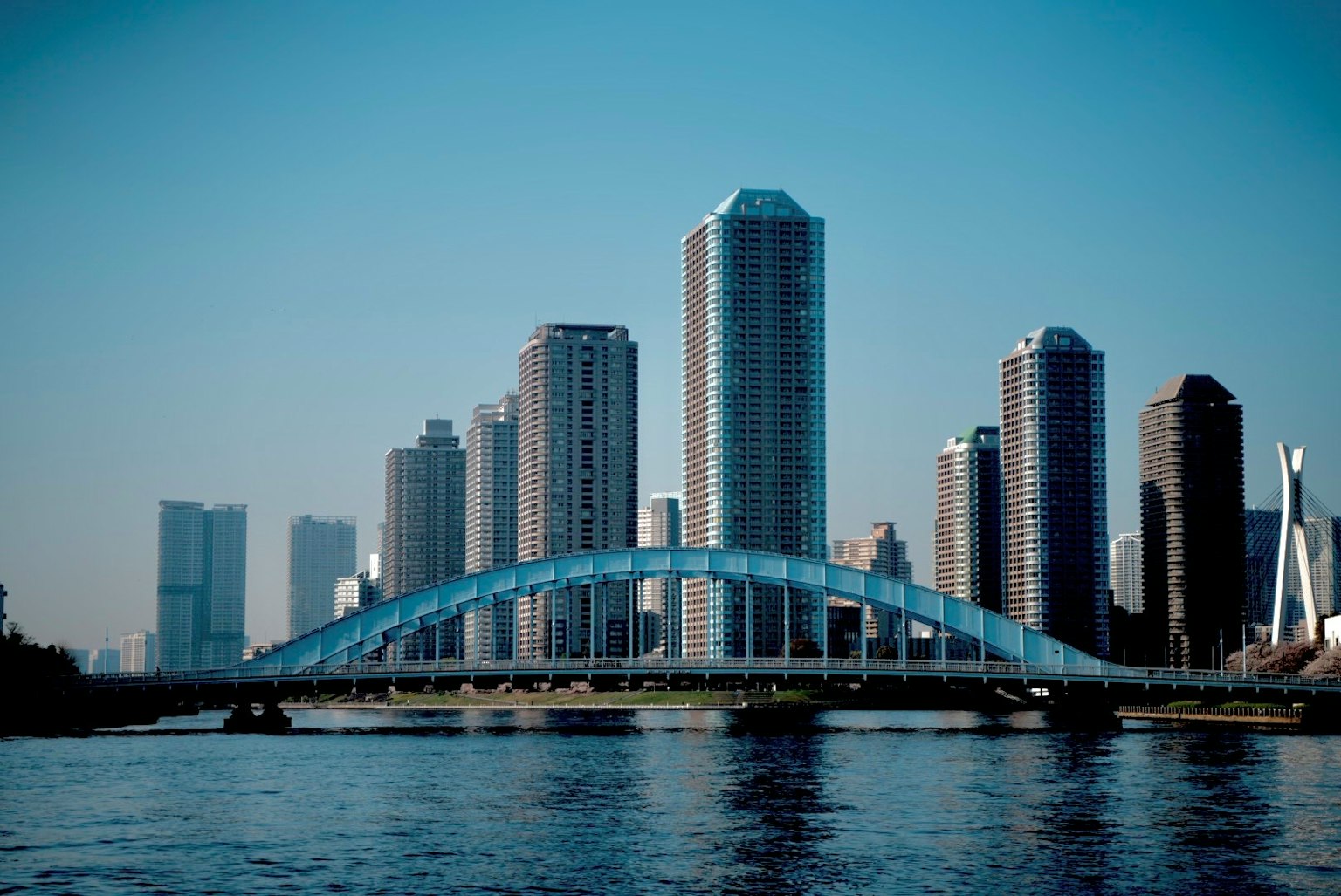 Garis langit kota dengan gedung tinggi dan jembatan lengkung biru di bawah langit cerah