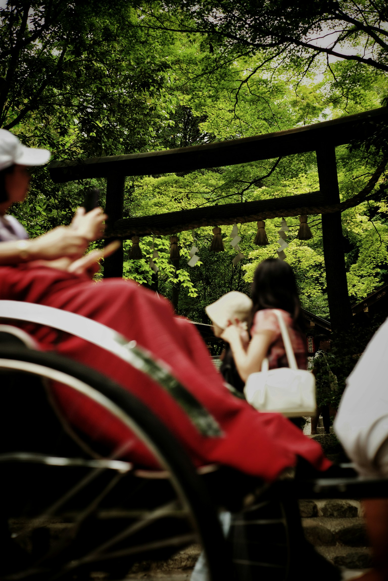 People in a serene setting with a torii gate and bells surrounded by lush greenery