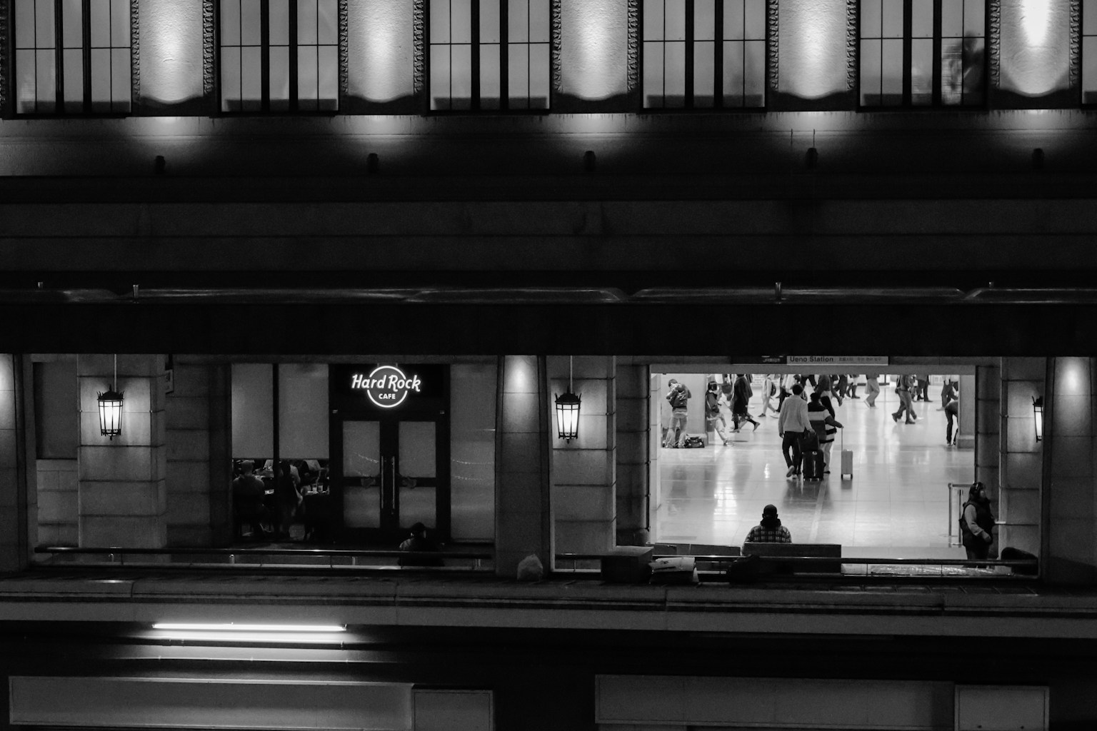 Extérieur en noir et blanc d'un bâtiment avec un panneau Hard Rock Cafe et des gens se rassemblant dans une place