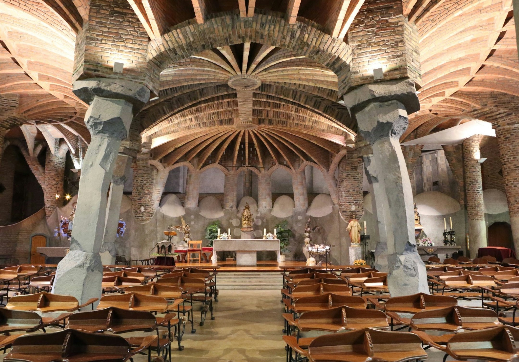 Intérieur de la crypte de la Colònia Güell avec rangées de chaises et autel