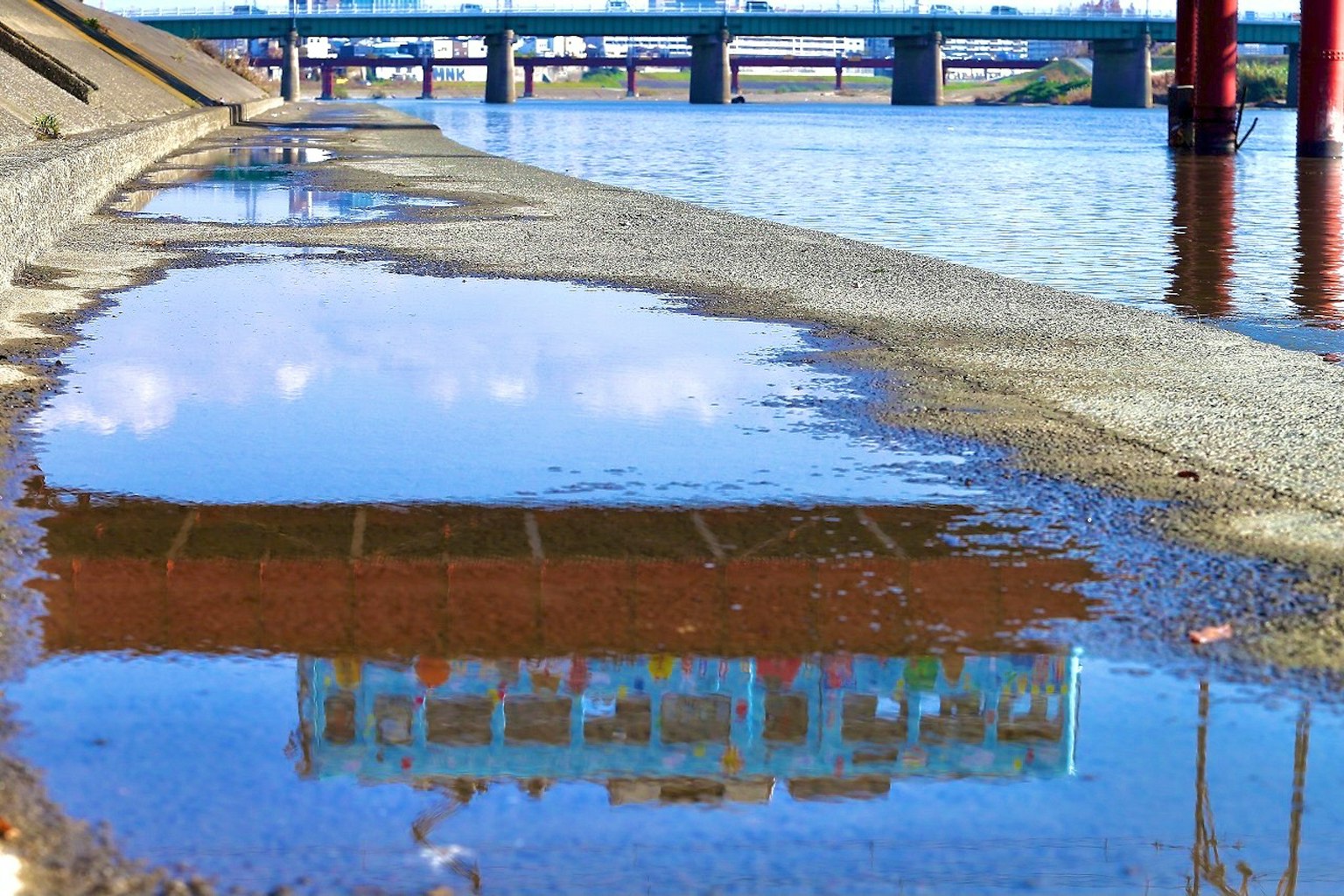 Reflet d'un pont dans une flaque d'eau au bord de la rivière et du rivage en béton