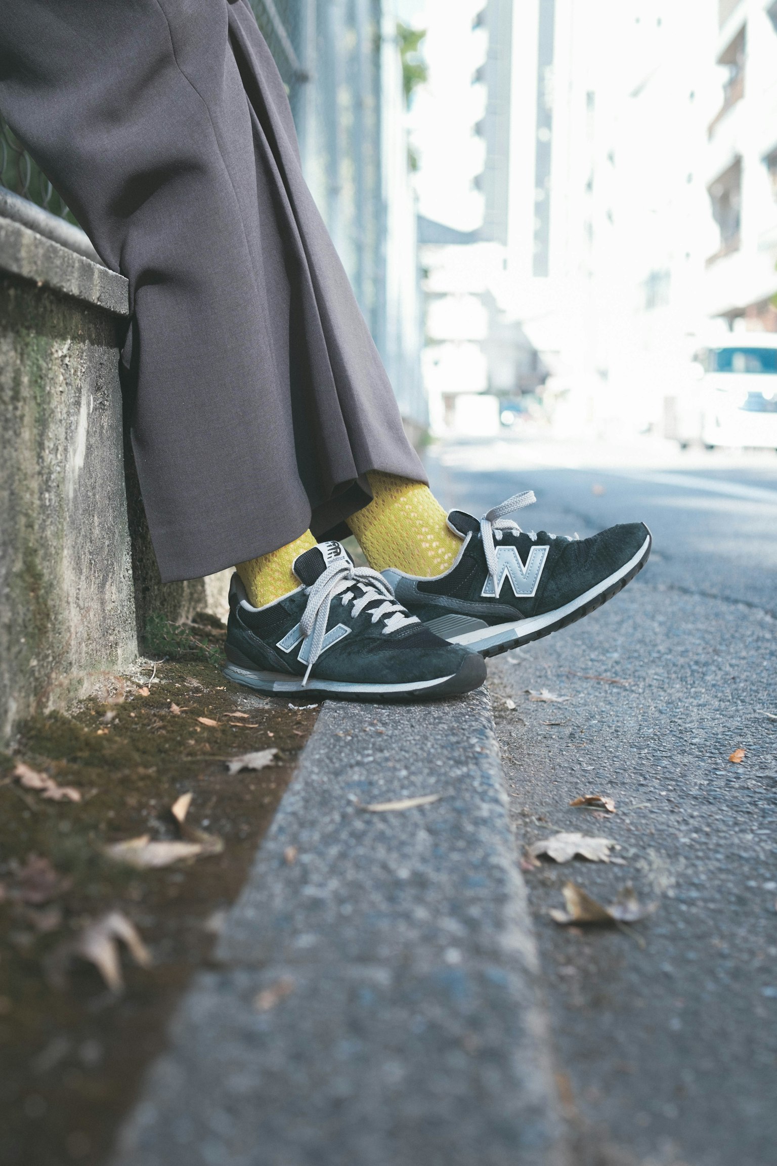 Füße in schwarzen New Balance Sneakers und gelben Socken auf dem Bürgersteig ruhend