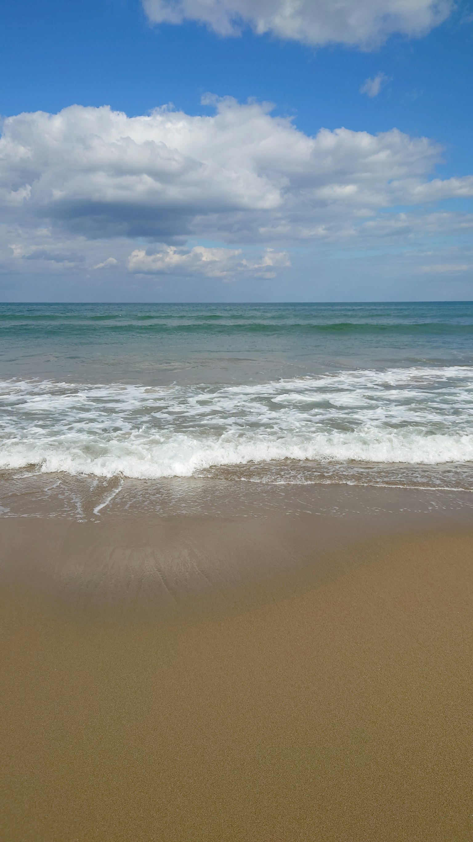 Strandszene mit Wellen, die unter einem blauen Himmel und weißen Wolken brechen
