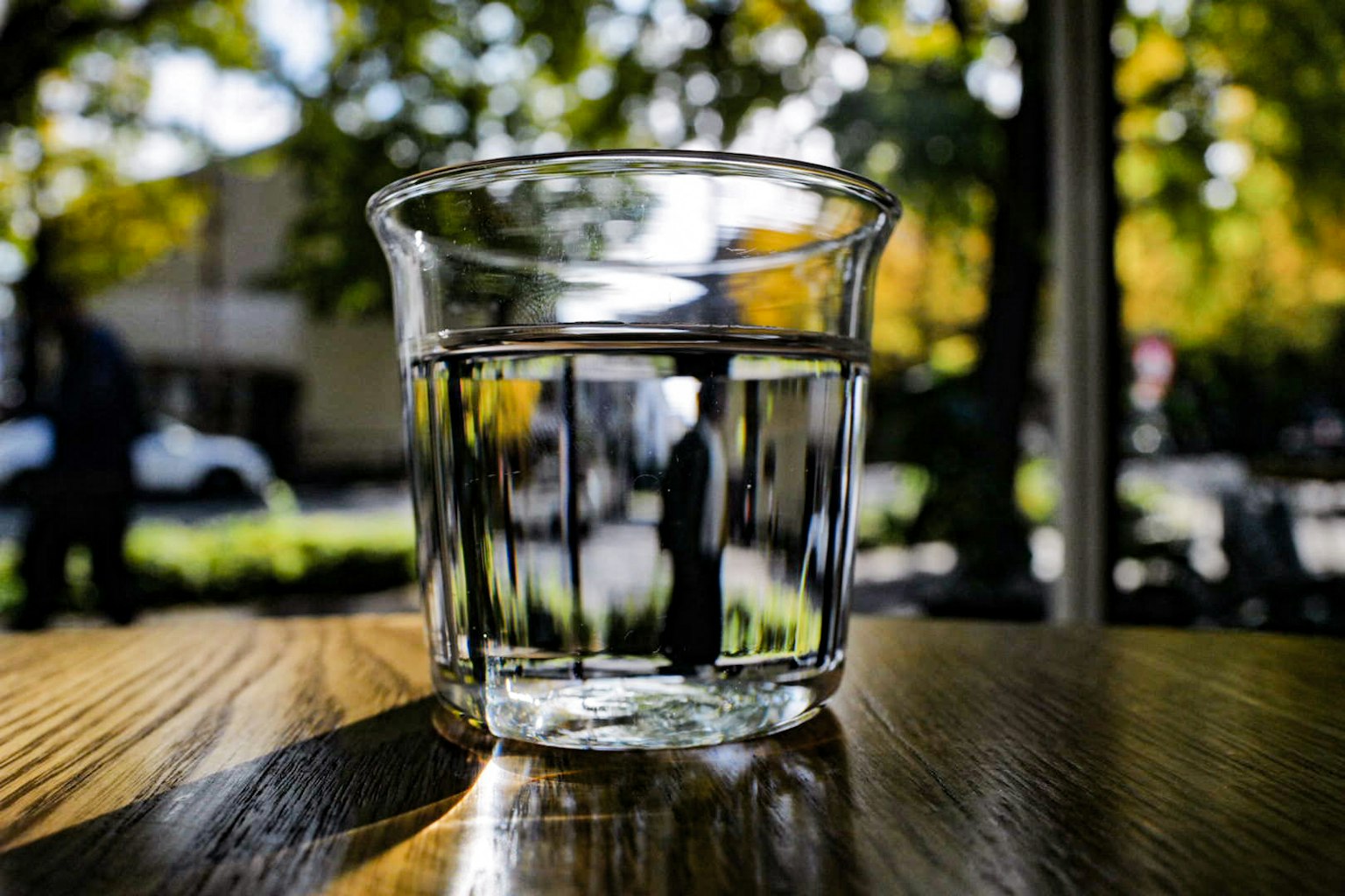 透明な水が入ったグラスが木のテーブルの上に置かれている背景には秋の木々が見える