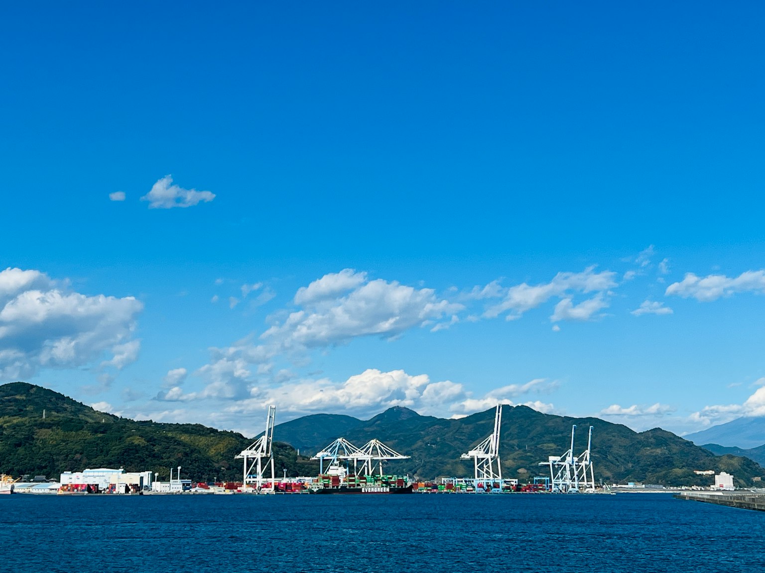 Landschaft mit Kränen im Hafen unter einem blauen Himmel und Bergen im Hintergrund