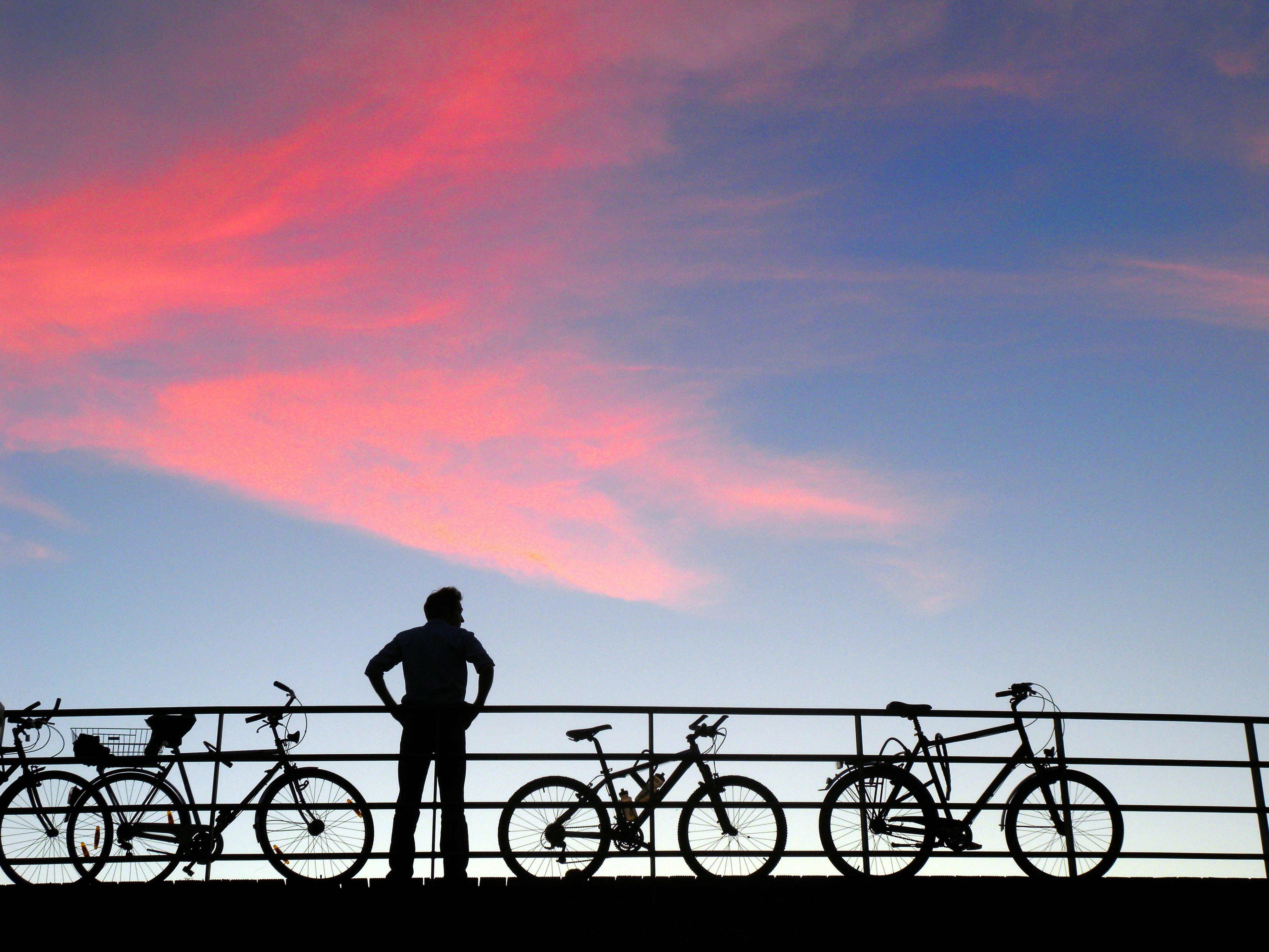 silhouette of a person and bicycles along a railing at sunset