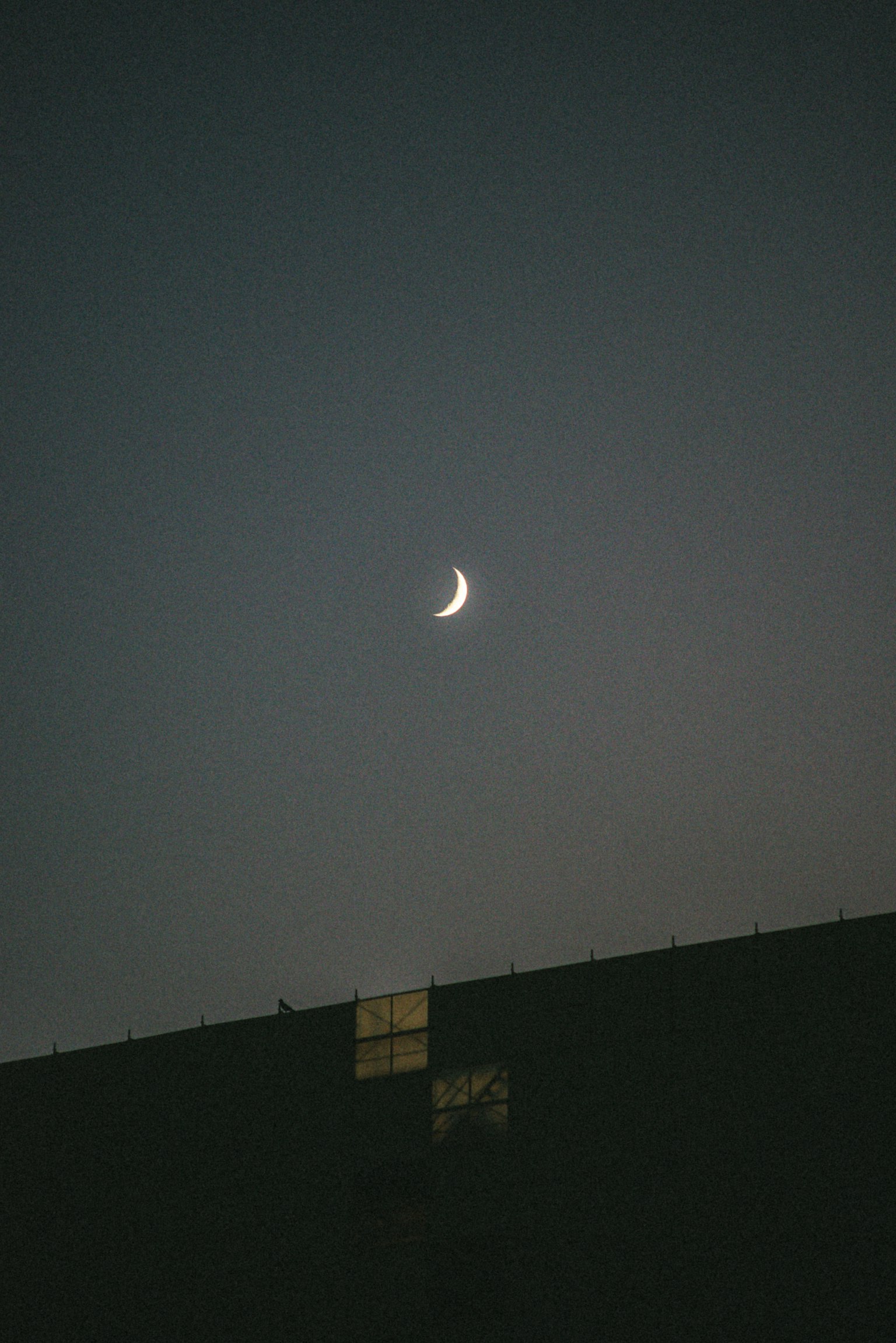 Sottile luna crescente in un cielo scuro con silhouette di edificio