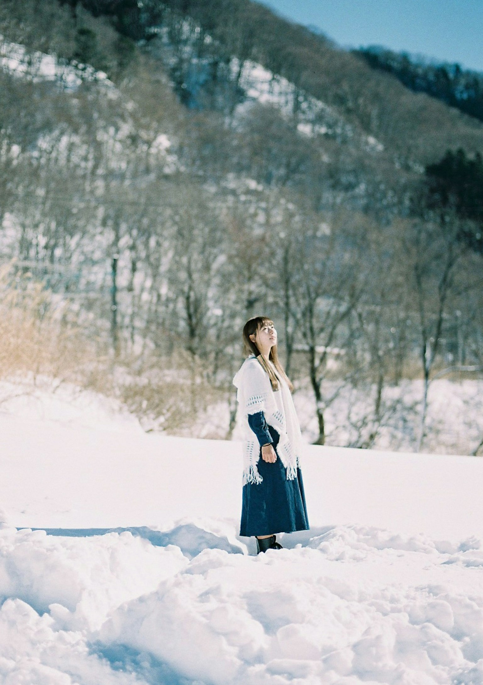 Frau steht im Schnee mit einem weißen Mantel und einem blauen Rock Winterlandschaft