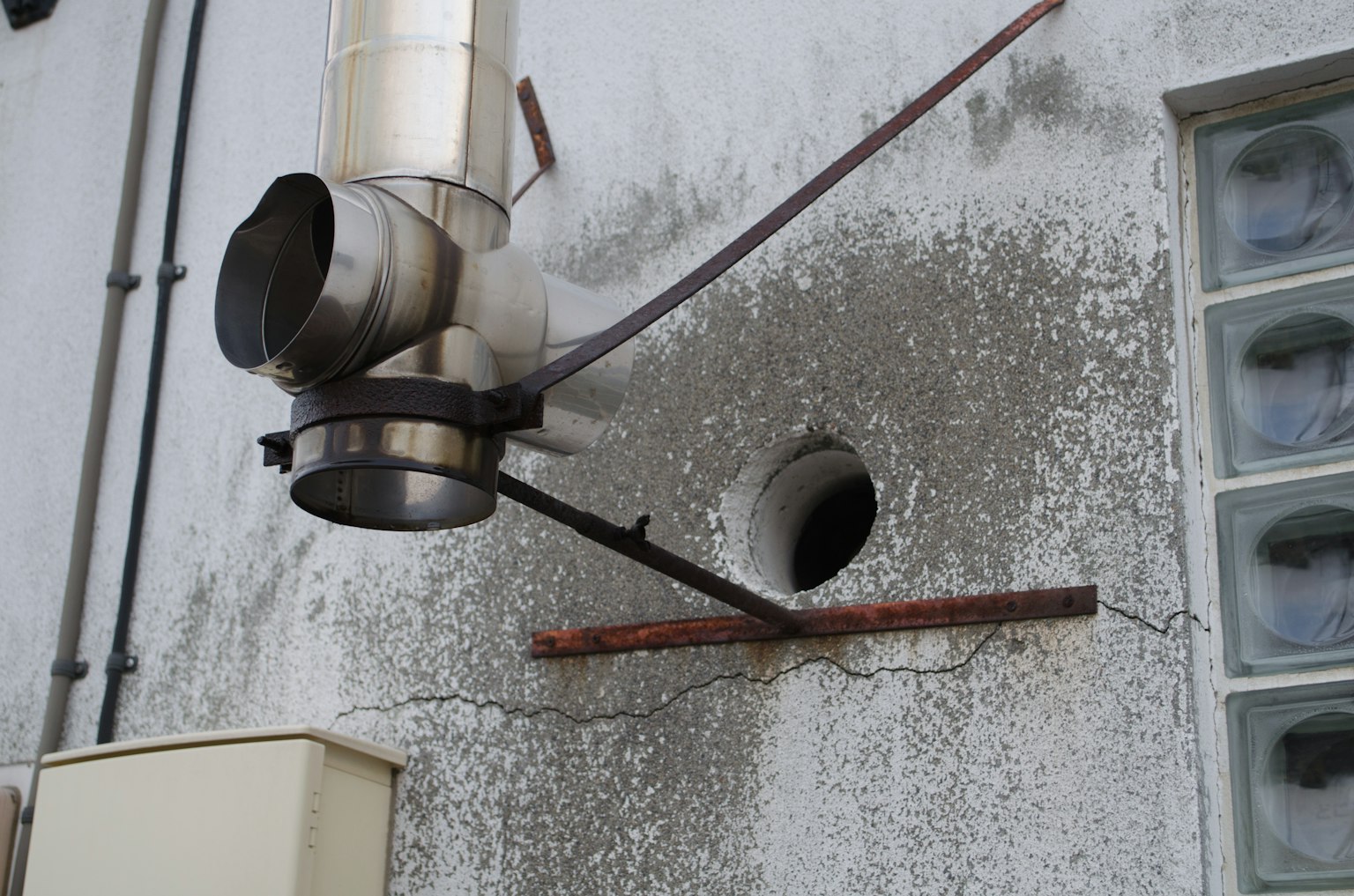 Immagine che mostra un camino in metallo attaccato a un muro con calcestruzzo invecchiato e blocchi di vetro visibili intorno