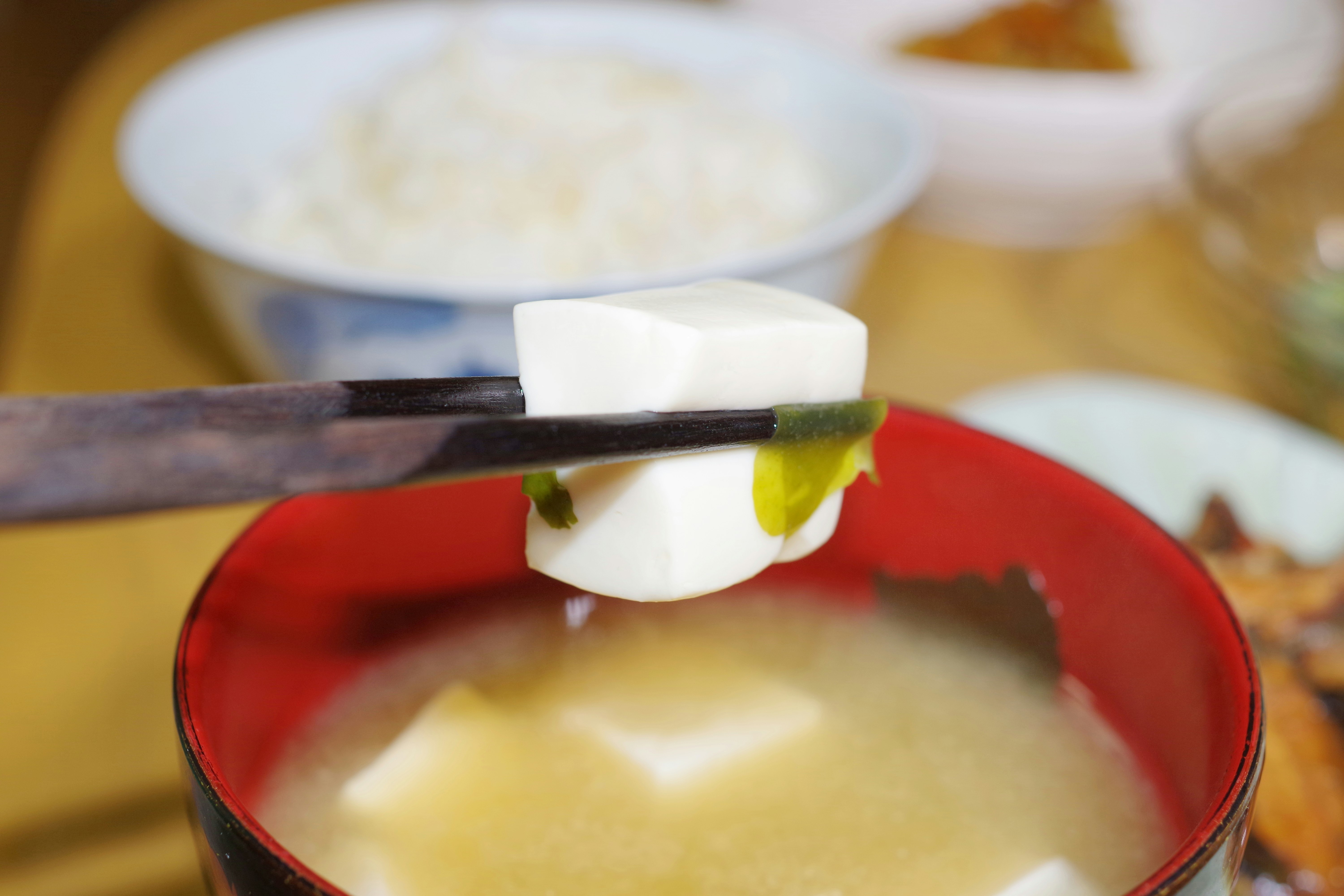 Chopsticks lifting tofu and seaweed from miso soup